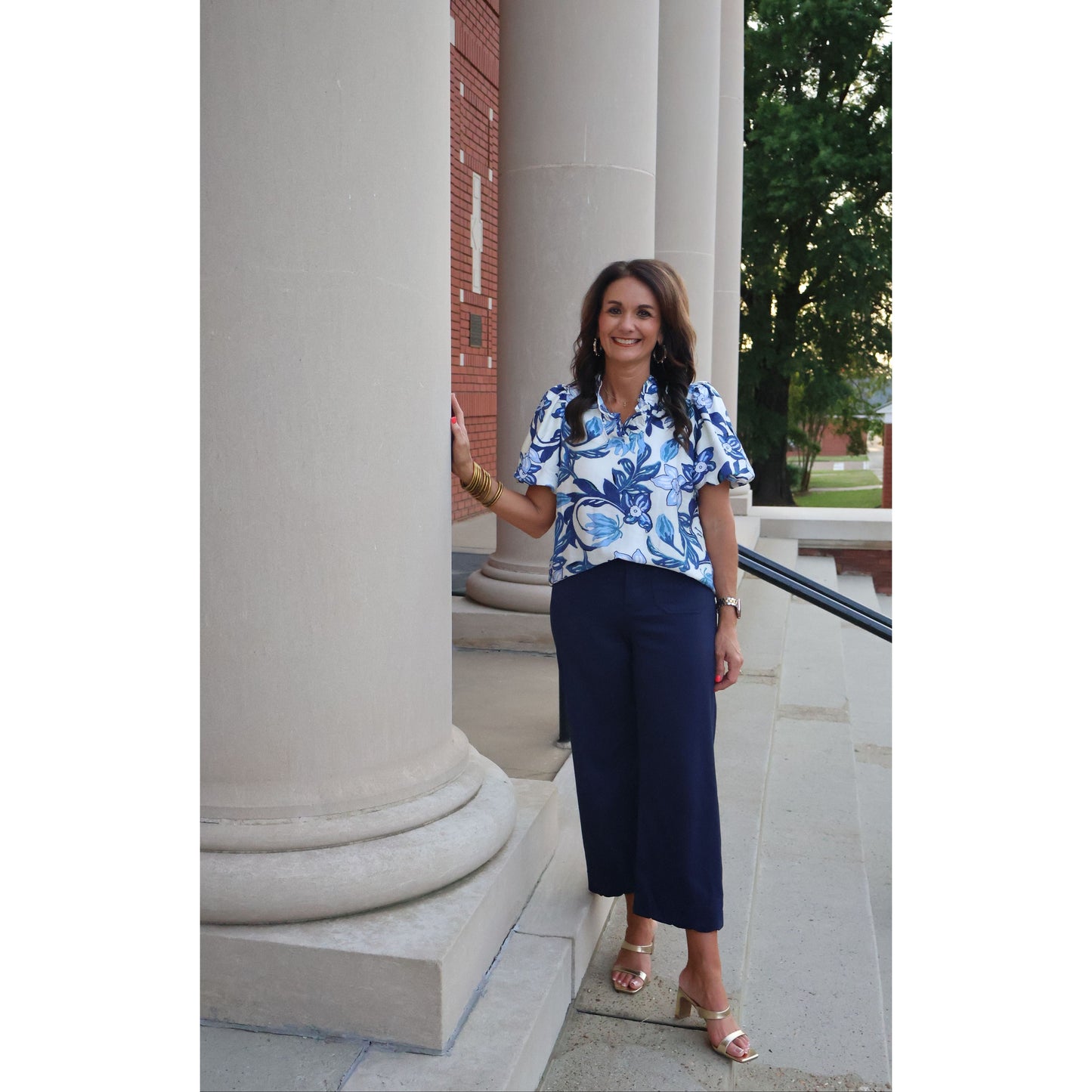 Woman in a blue floral dress and navy pants standing in front of a building with columns.