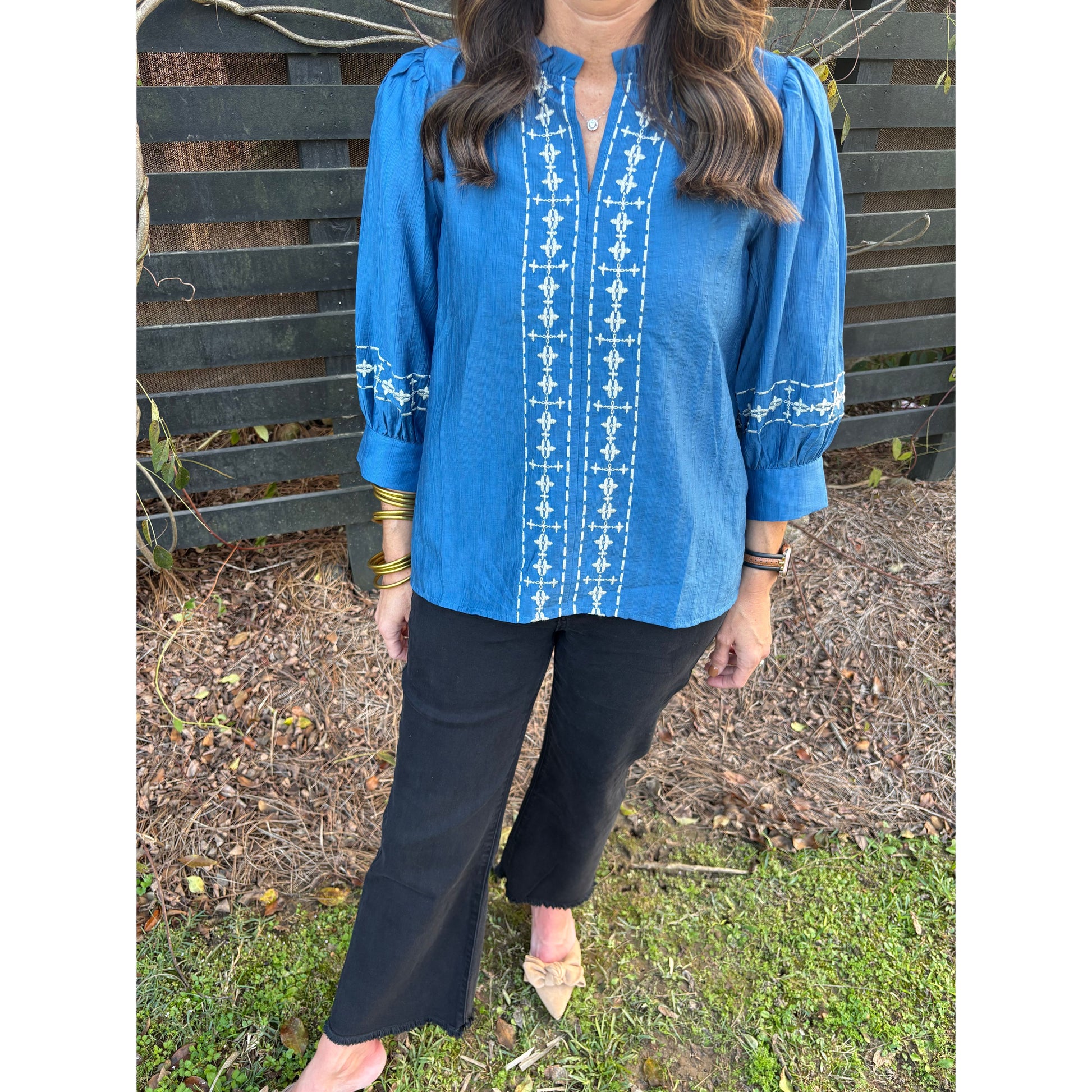 Person wearing a blue garment with white patterns sitting on a bench outdoors.