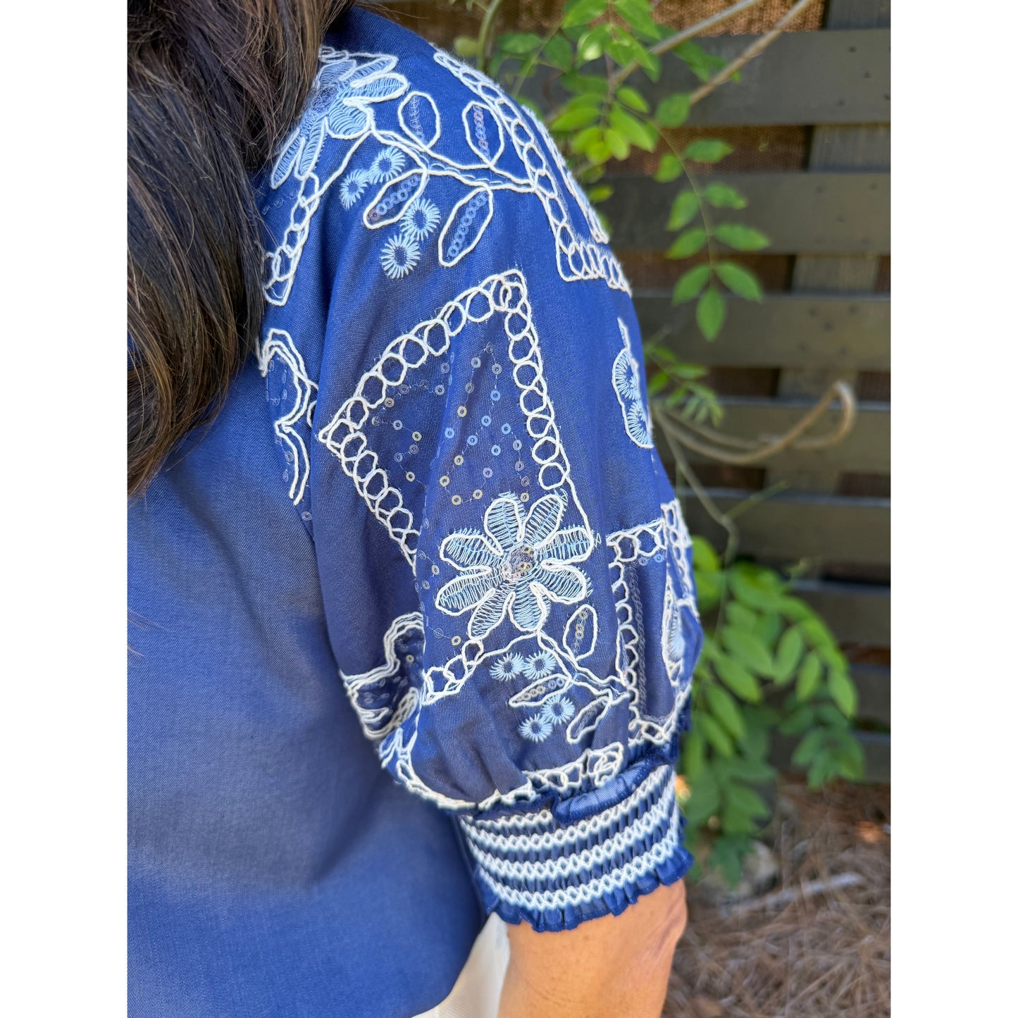 Blue embroidered garment with white patterns against a natural background