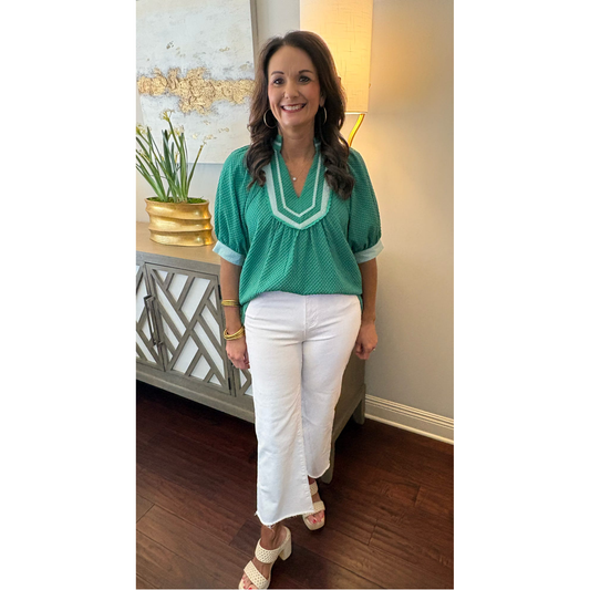Woman wearing a green blouse and white pants indoors.