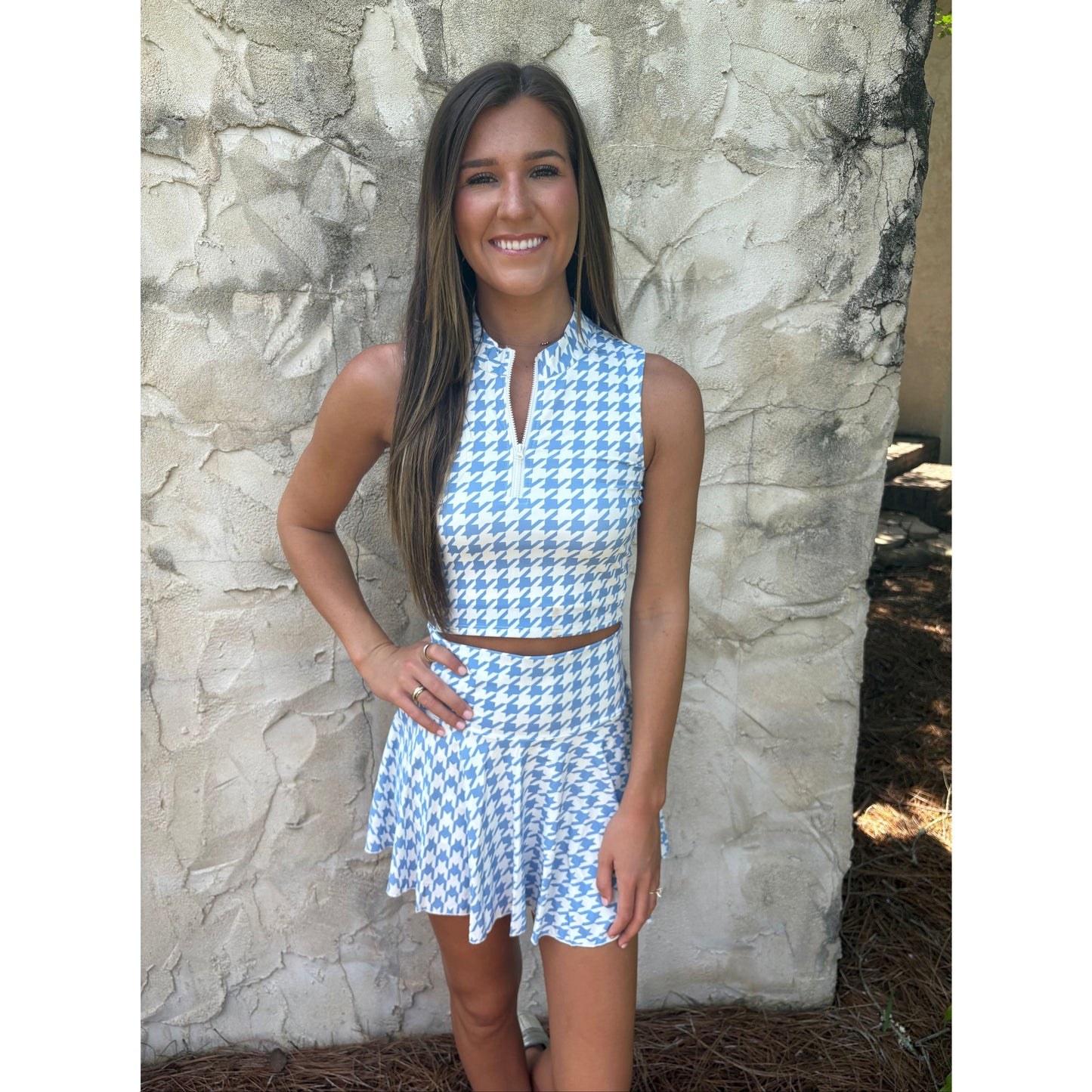 Woman wearing a blue and white checkered dress standing against a stone wall.