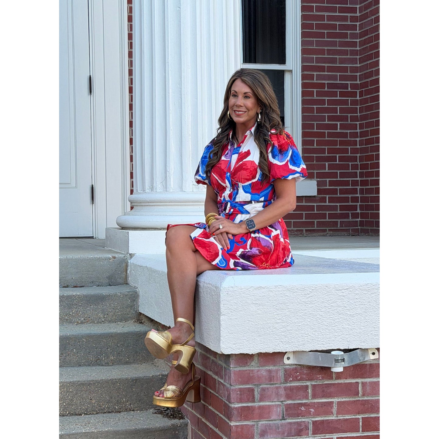 Woman in a colorful dress standing on steps with a brick building in the background