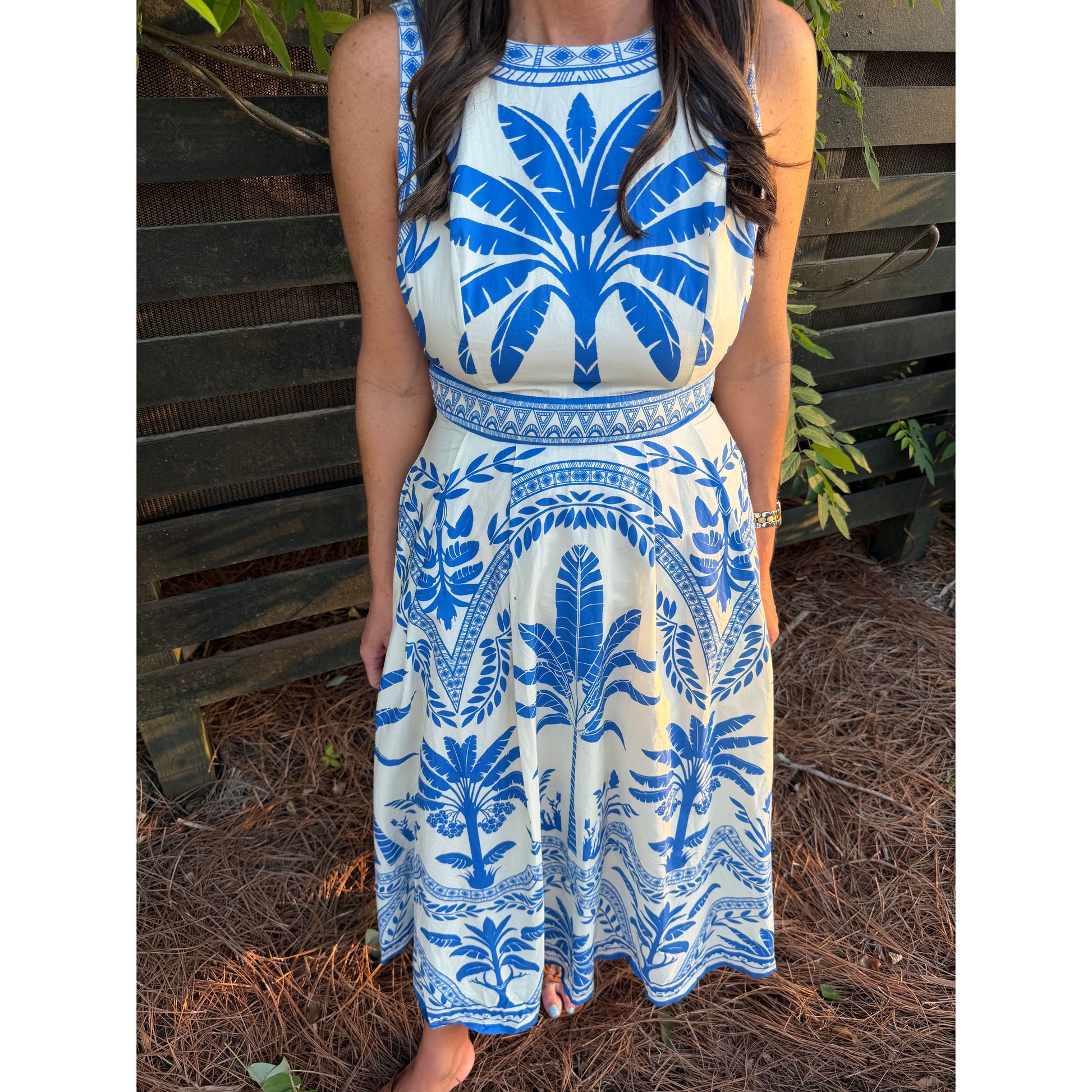 Woman wearing a blue and white patterned dress standing against a wooden fence.