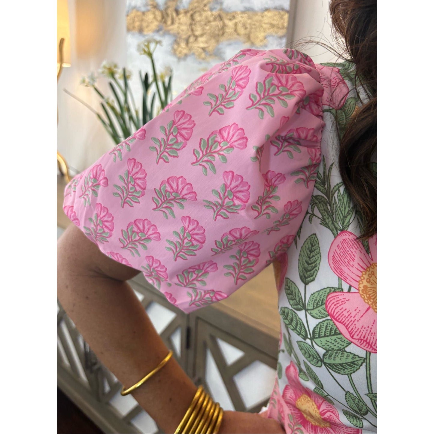 Person wearing a pink floral shower cap indoors with decorative elements in the background.