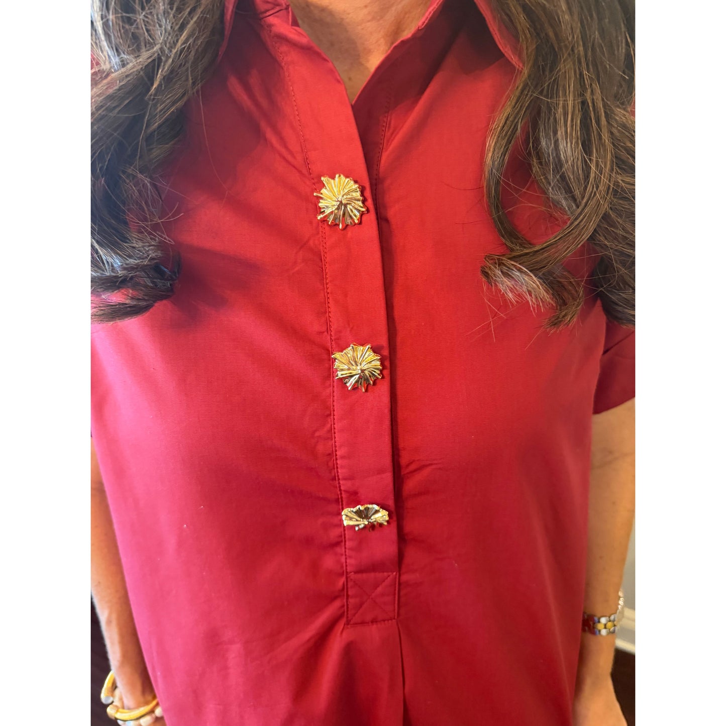 A close-up of a person wearing a red short-sleeve button-up shirt with three decorative gold flower-shaped buttons down the front placket.