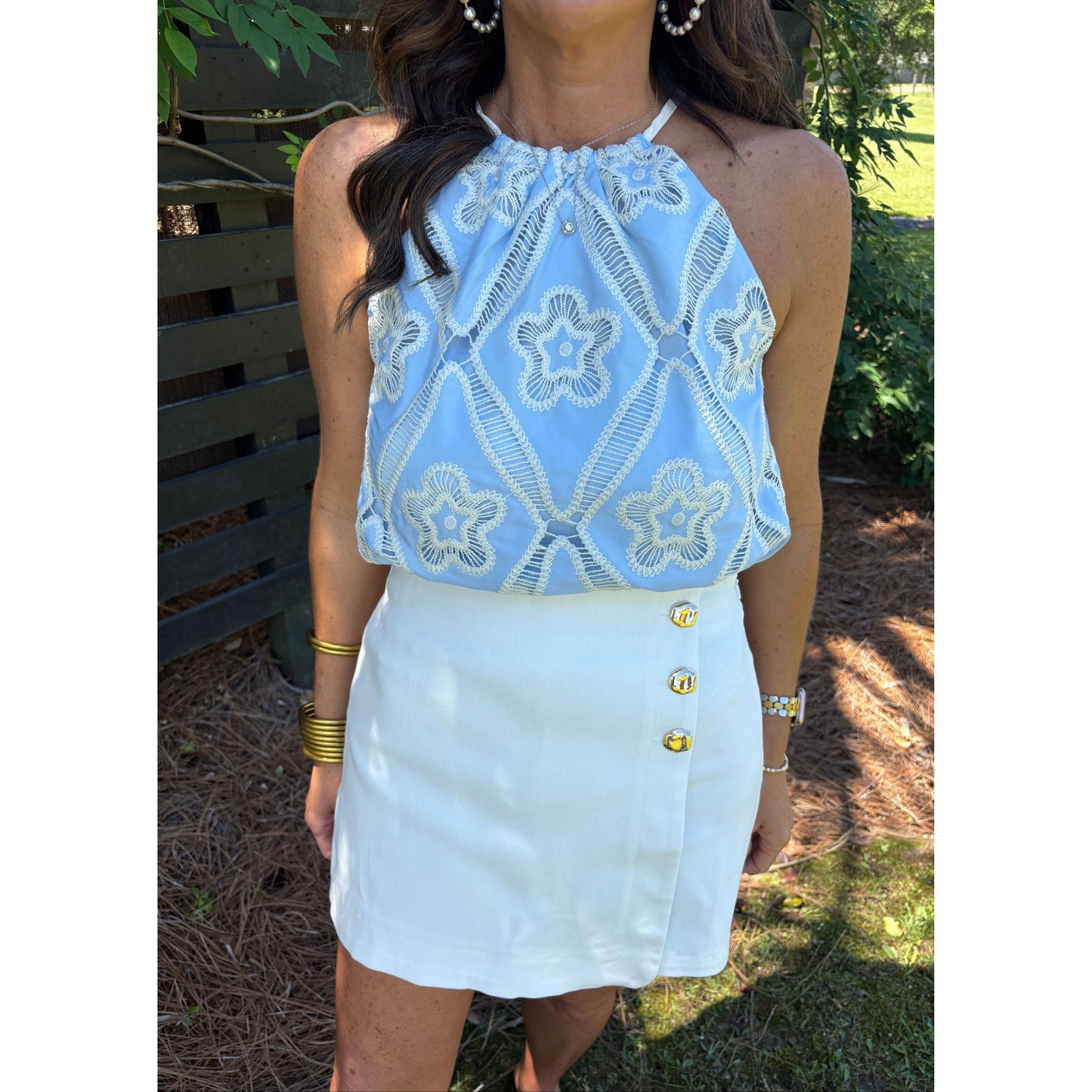 Person wearing a light blue lace top and white shorts outdoors.