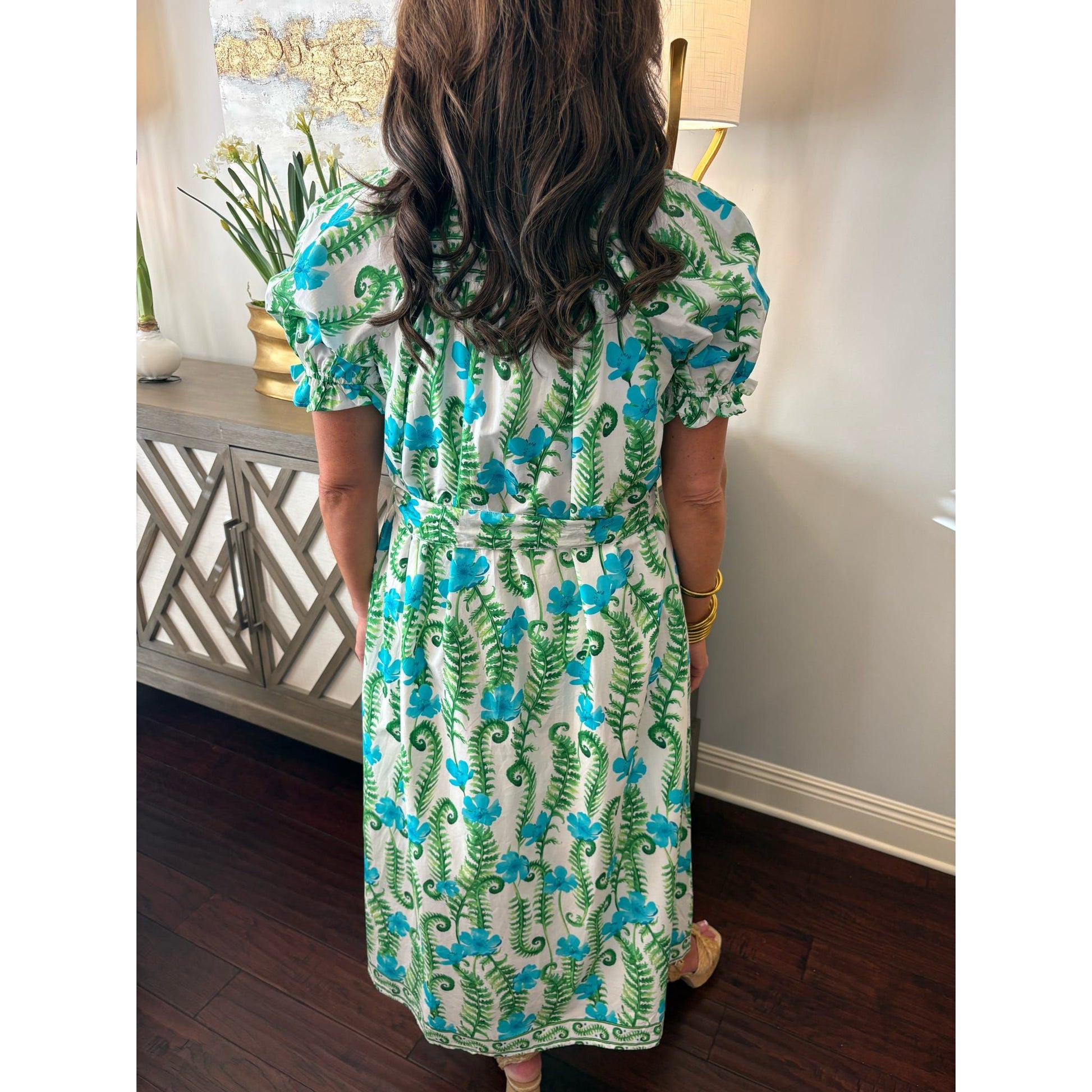 Person wearing a floral dress in a room with a lamp and plant.