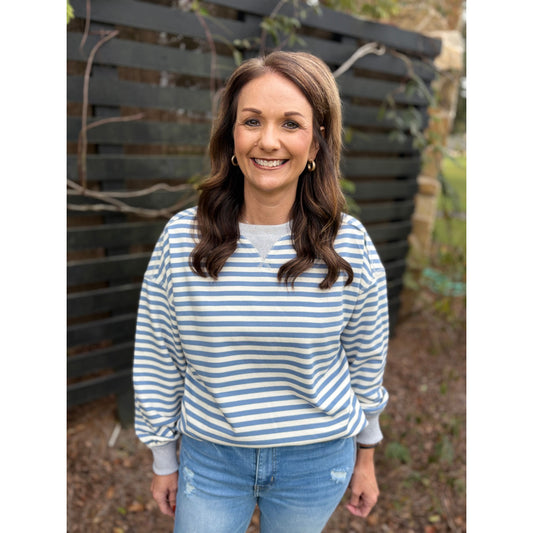 Woman wearing a blue and white striped shirt and jeans standing in front of a wooden fence.