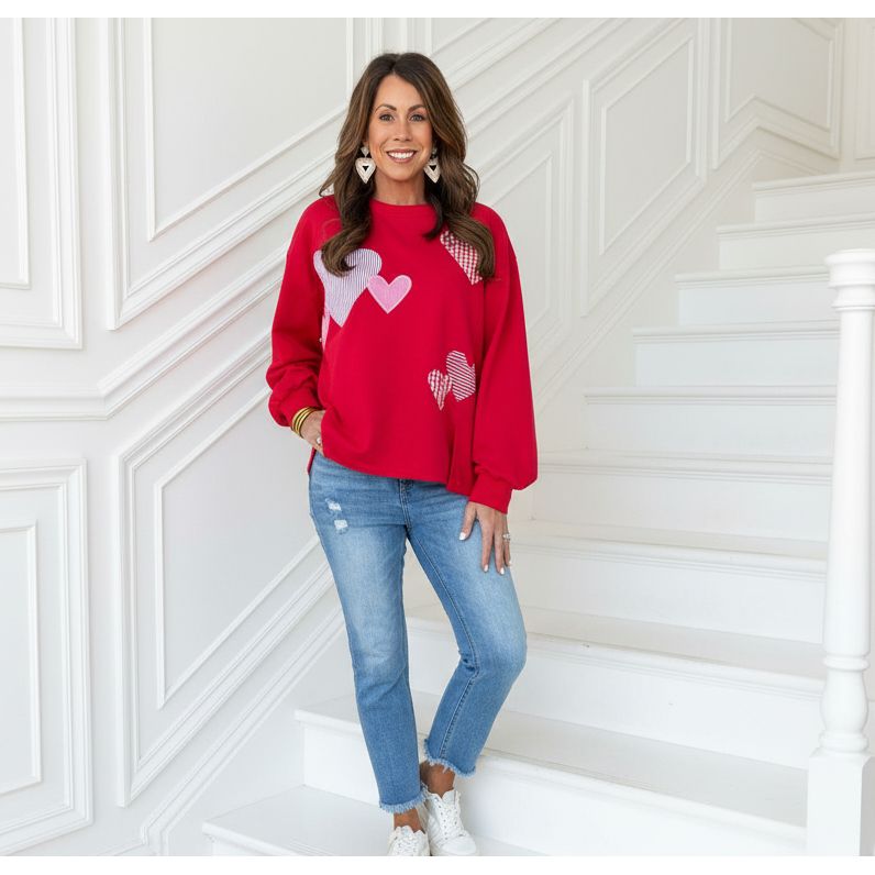 Woman wearing a red sweater with heart patterns standing on a staircase.
