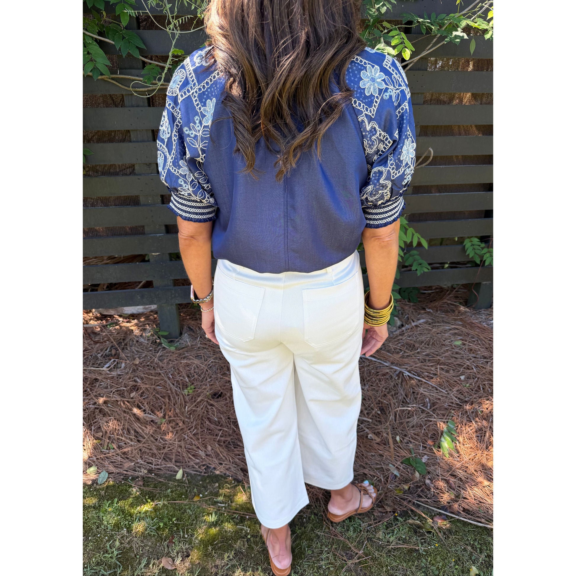Person wearing a blue shirt and white pants sitting on the ground with plants and soil in the background