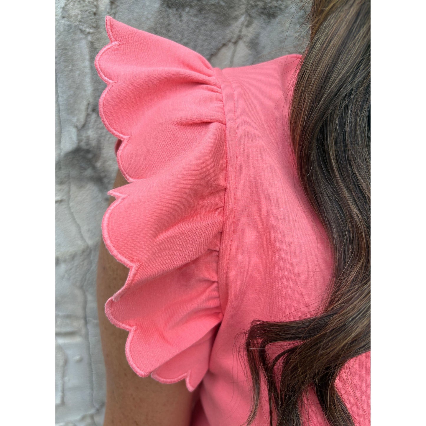 Close-up of a pink top with ruffled shoulders against a stone wall.
