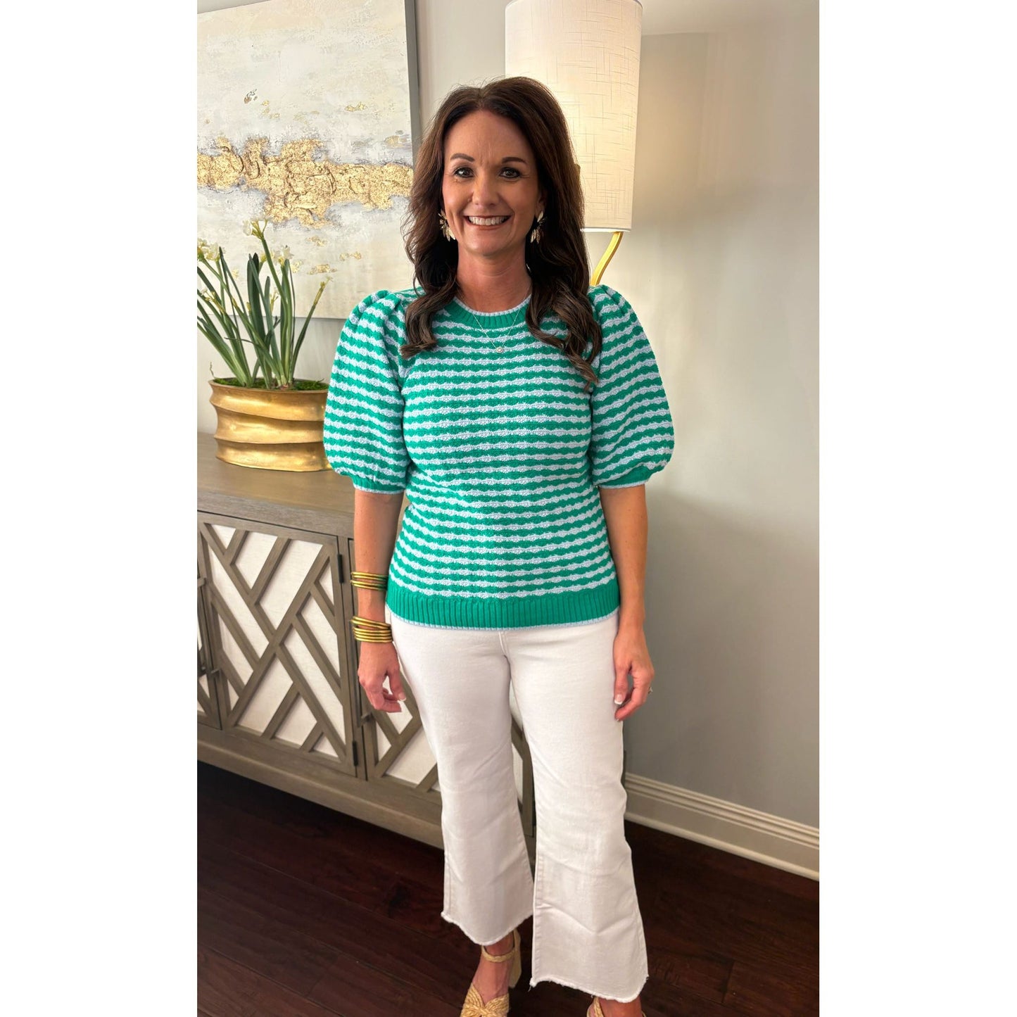 Woman wearing a green and white striped sweater and white pants indoors.