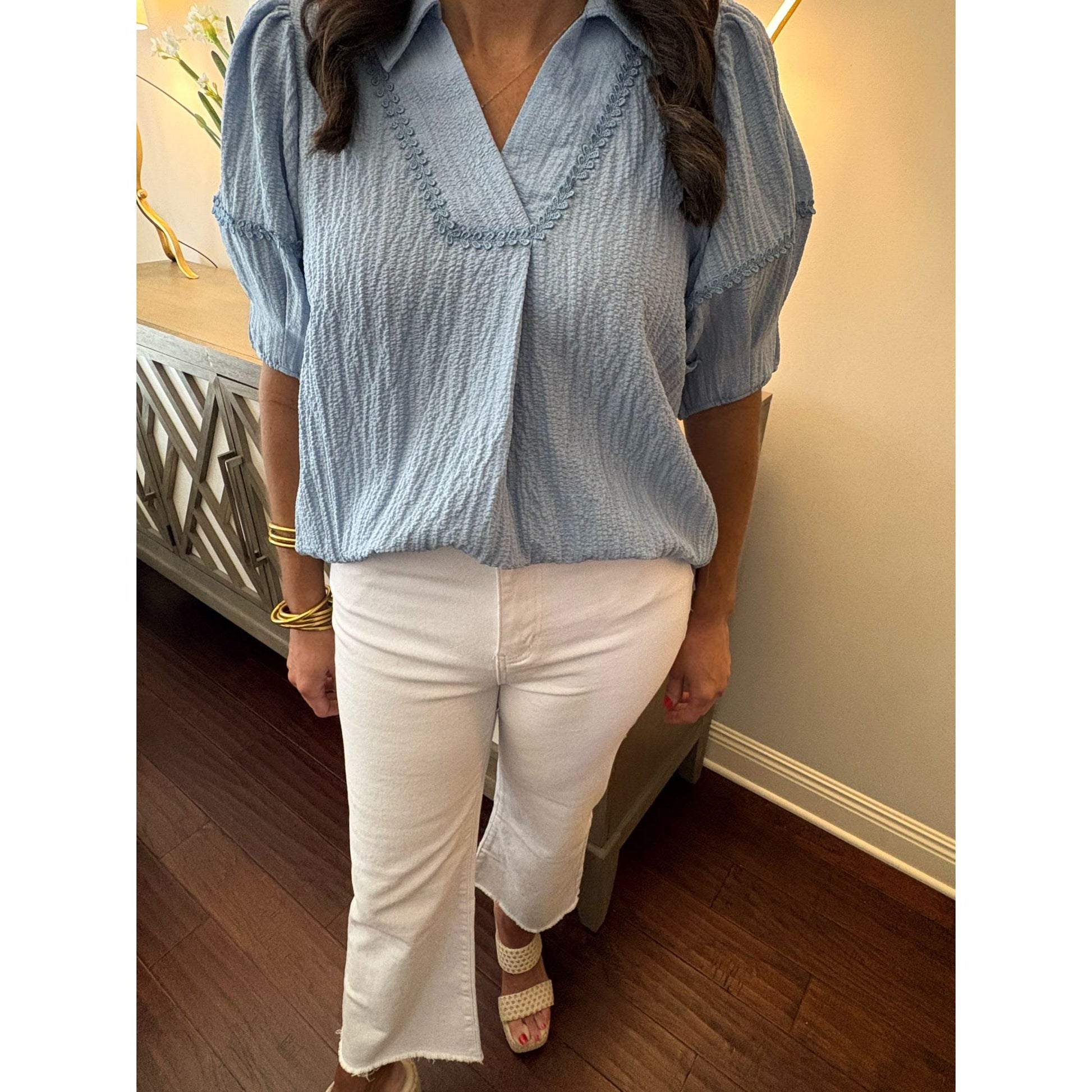 Person wearing a light blue blouse and white pants indoors.