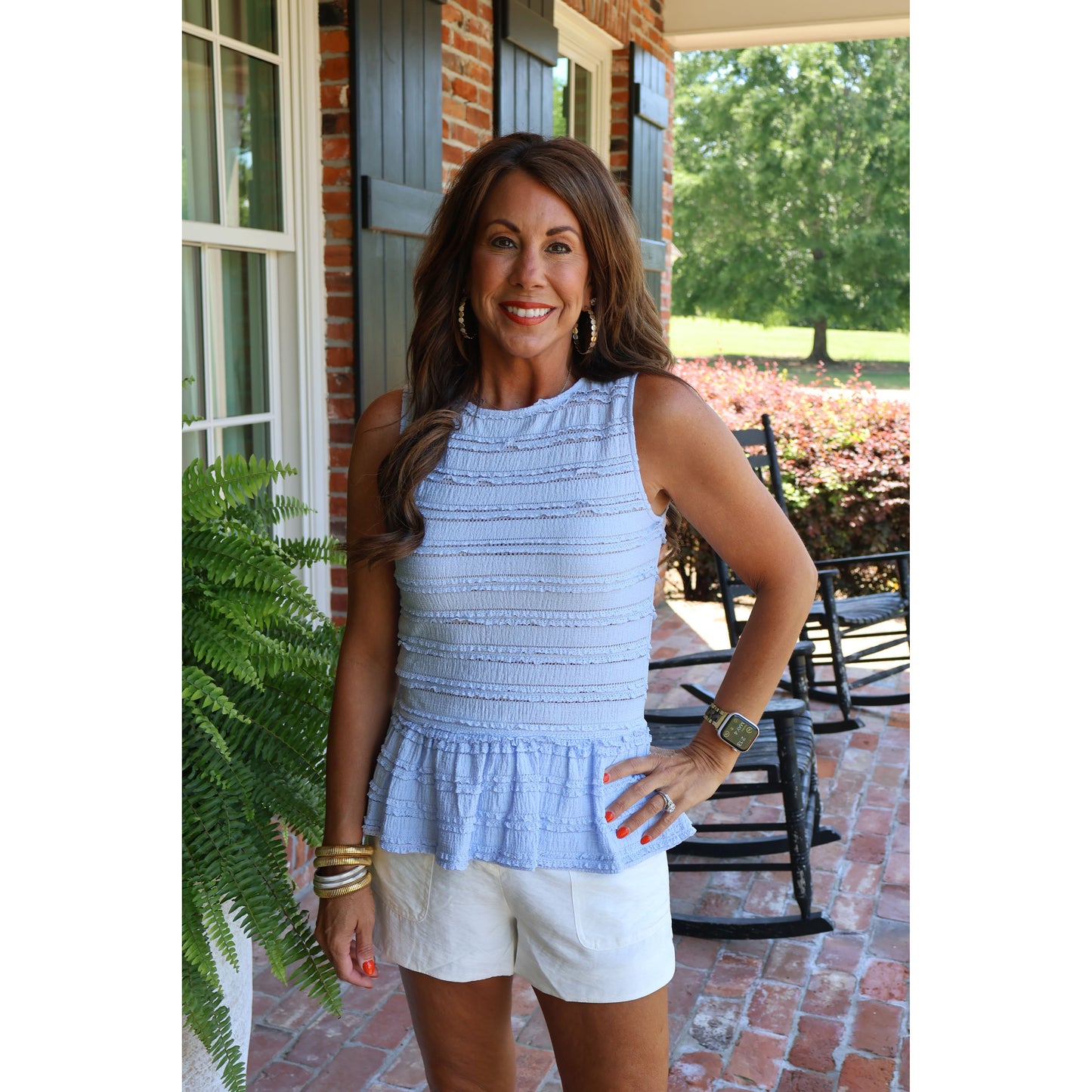 Woman in a light blue sleeveless top and white shorts standing on a patio.