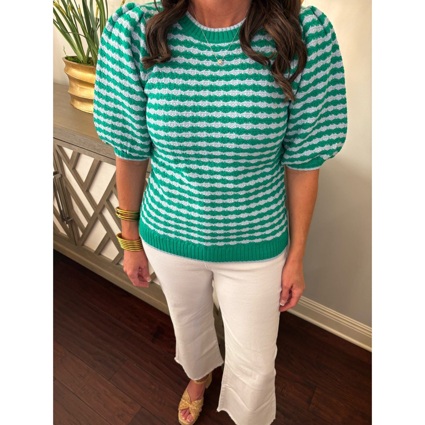 Person wearing a green and white striped sweater and white pants indoors.
