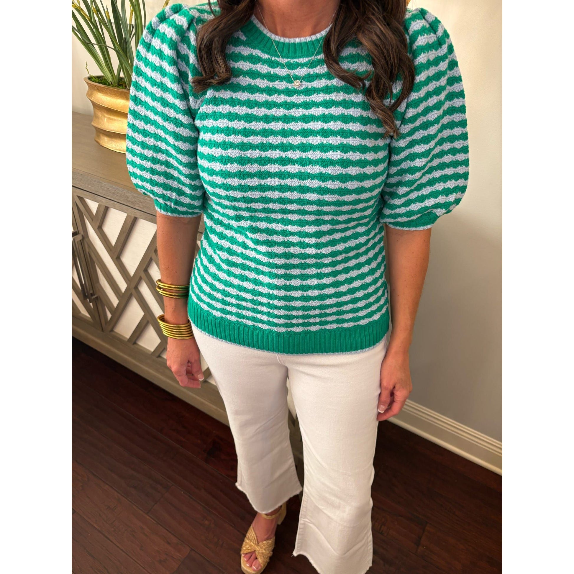 Person wearing a green and white striped sweater and white pants indoors.