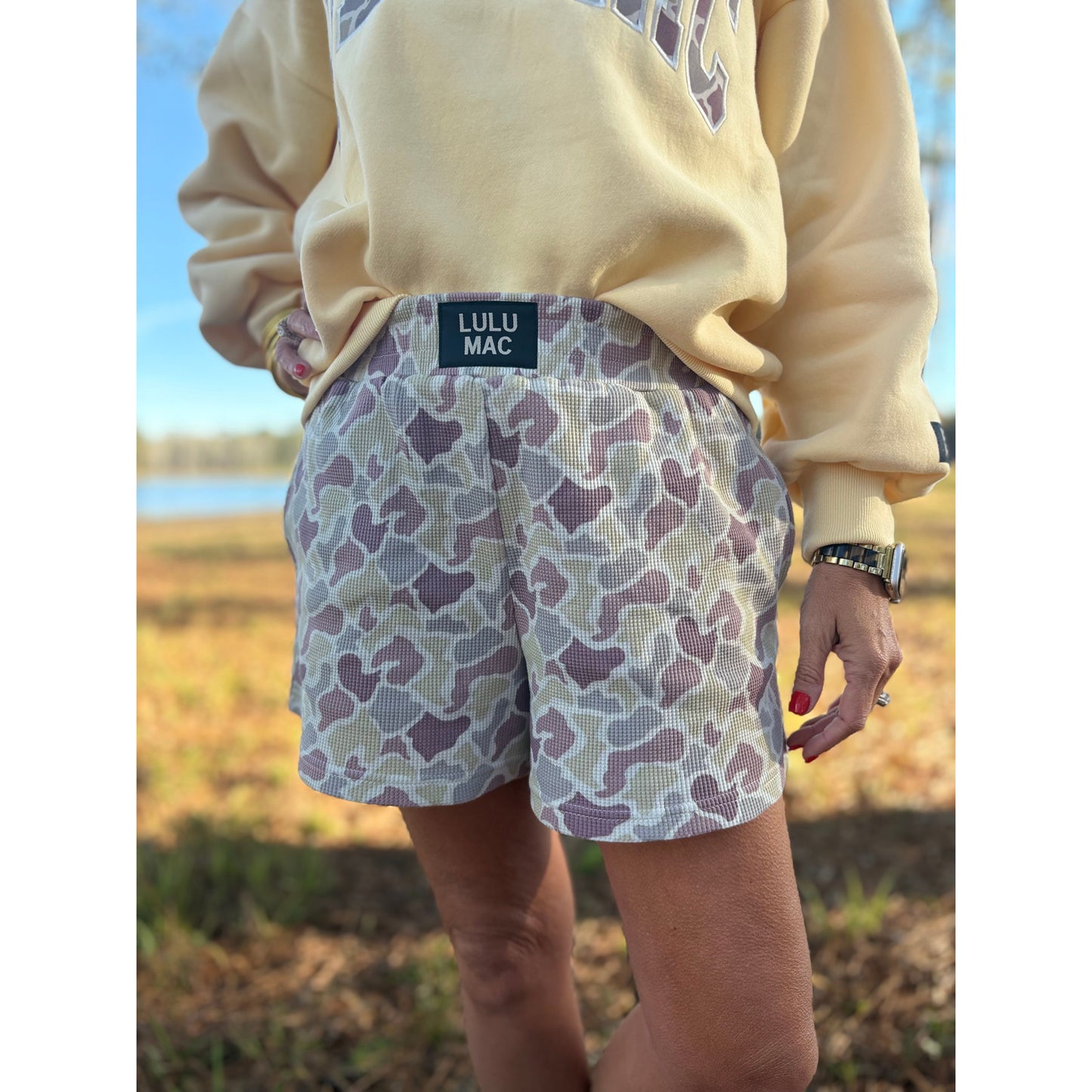Person wearing a beige sweatshirt and patterned shorts with LULU MAC branding outdoors.