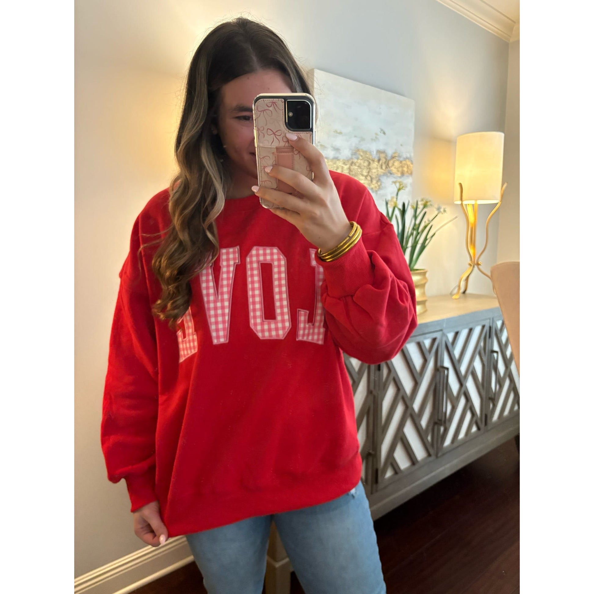 Person wearing a red sweatshirt with 'LOVE' text, taking a mirror selfie.