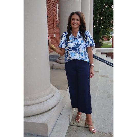 Woman in a blue floral blouse and navy pants standing outdoors.