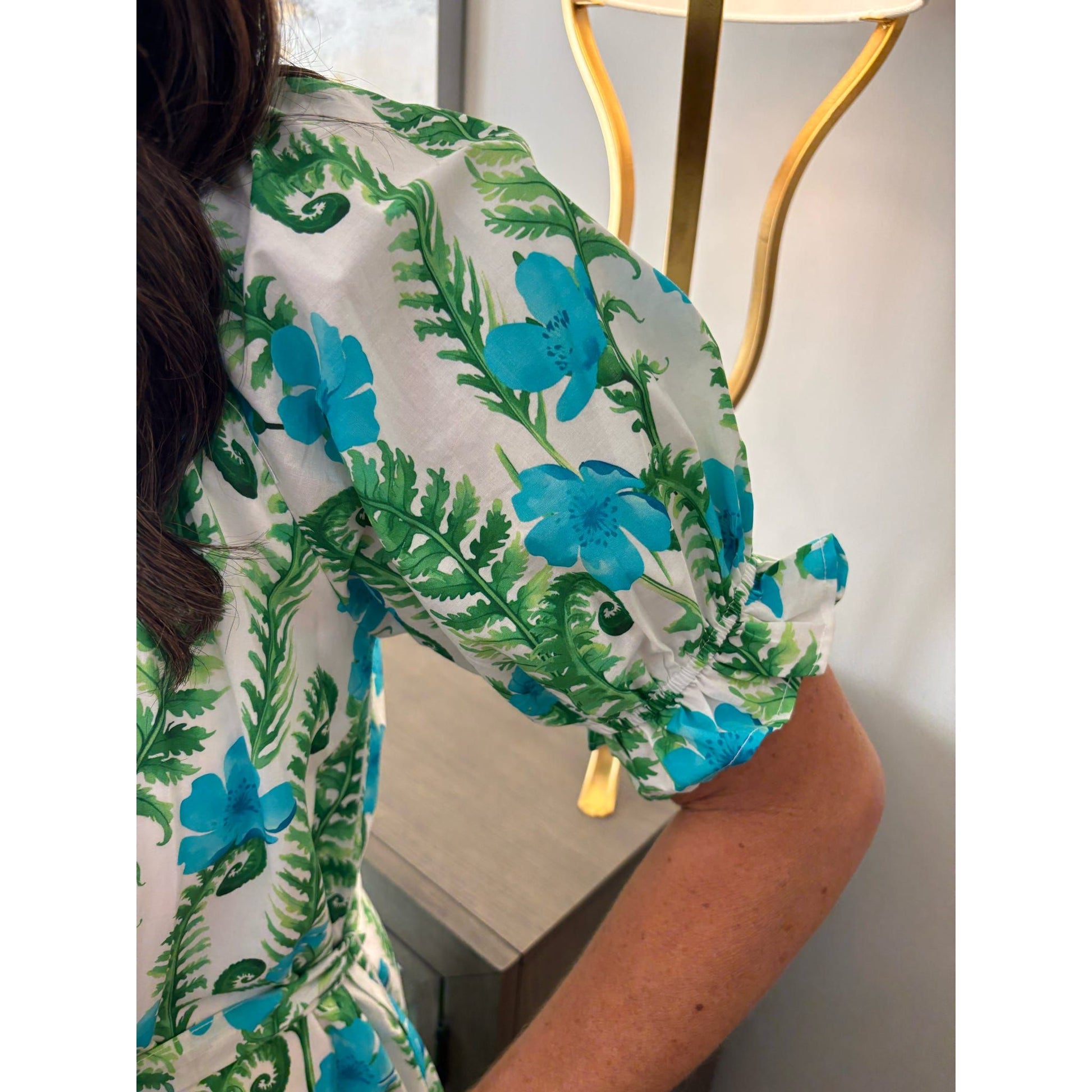 Person wearing a floral dress with blue flowers and green leaves.