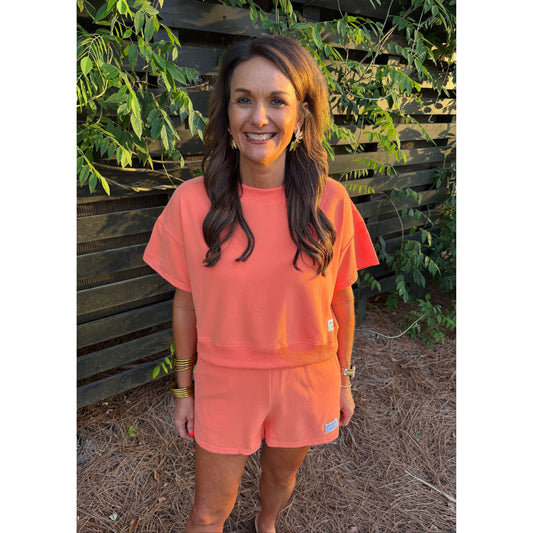 Woman wearing a coral outfit standing outdoors with greenery in the background