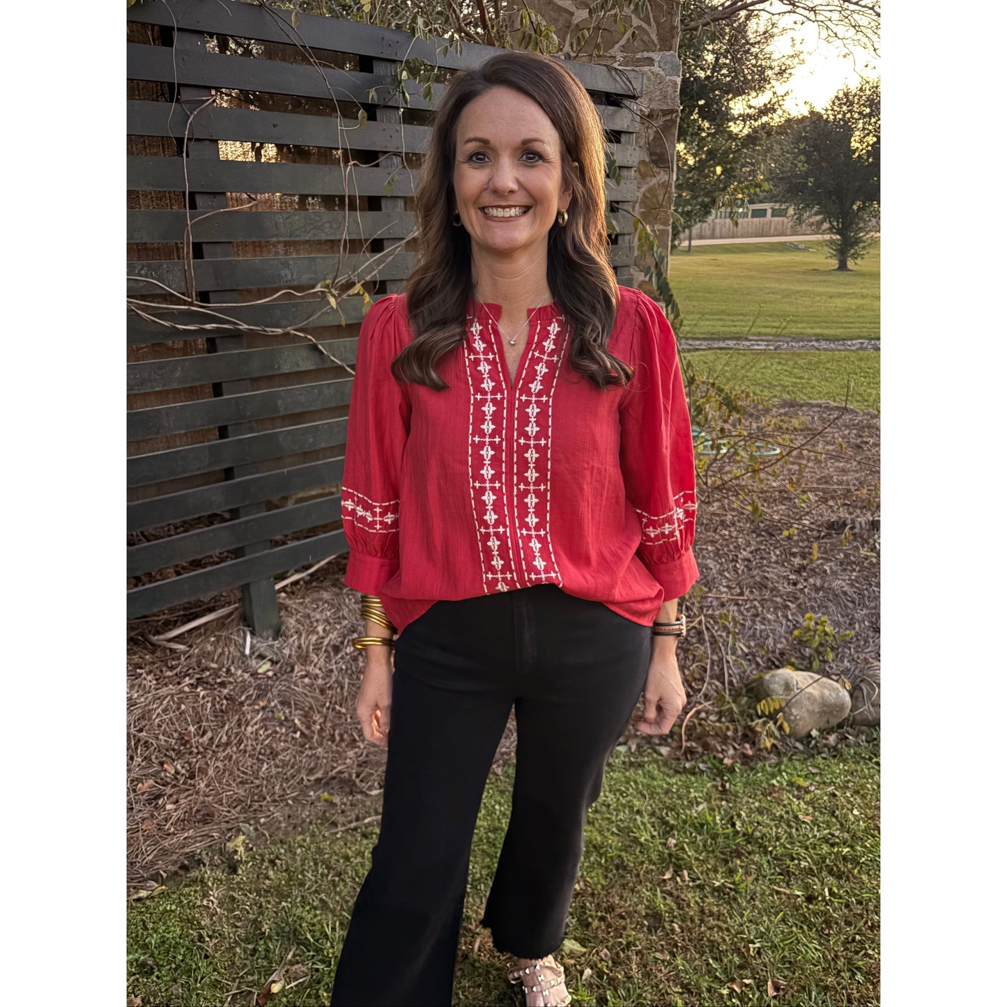 Person wearing a red sweater with white patterns standing outdoors near a wooden bench.