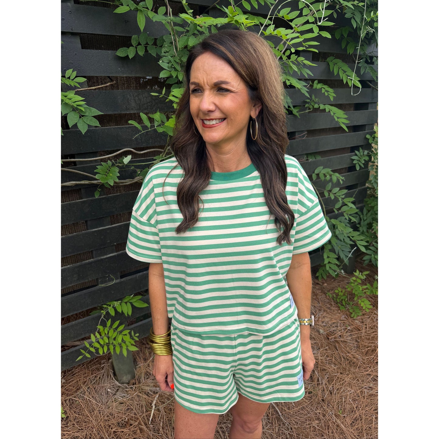Woman wearing a green and white striped dress standing outdoors with plants around.