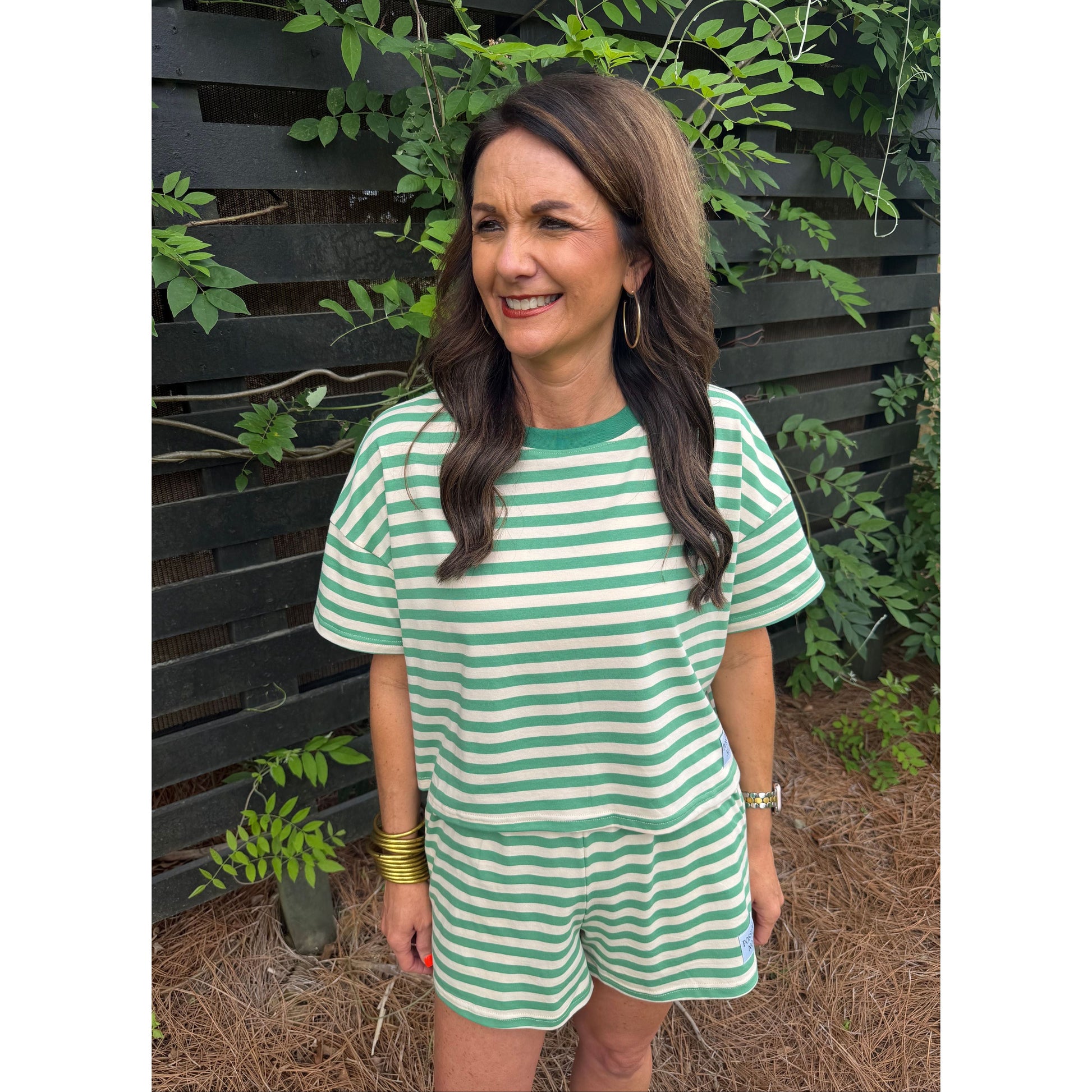 Woman wearing a green and white striped dress standing outdoors with plants around.