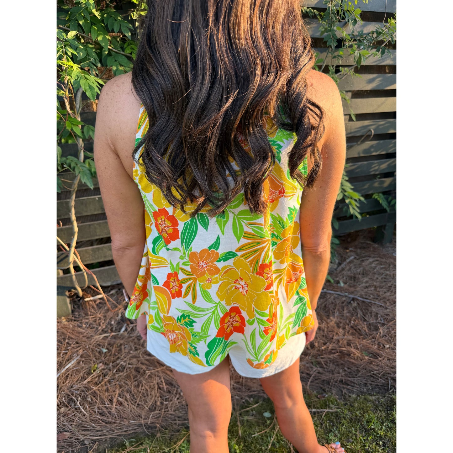 Person wearing a colorful floral top standing outdoors with greenery in the background