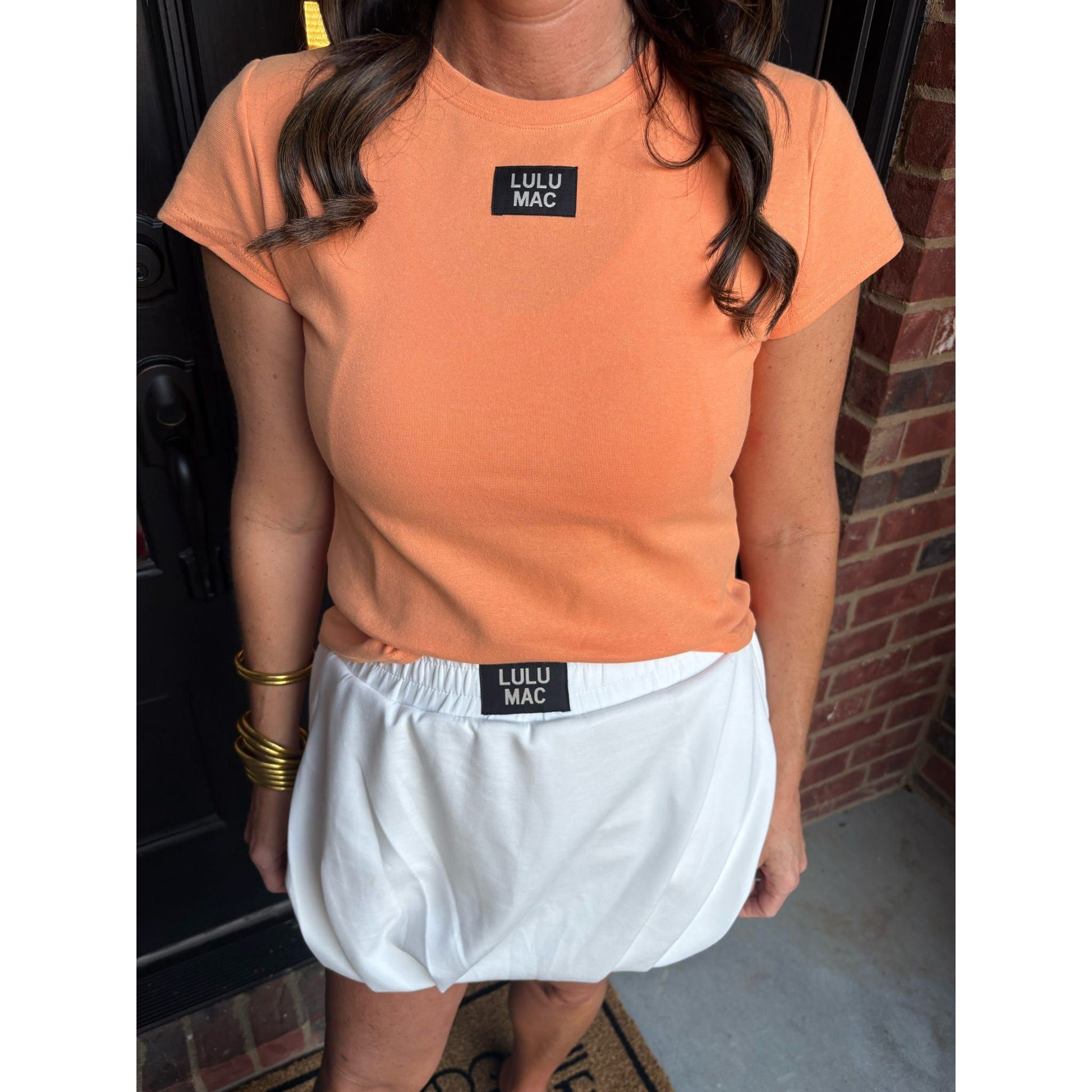 Person wearing an orange t-shirt and white shorts with 'Lulu Mac' branding.