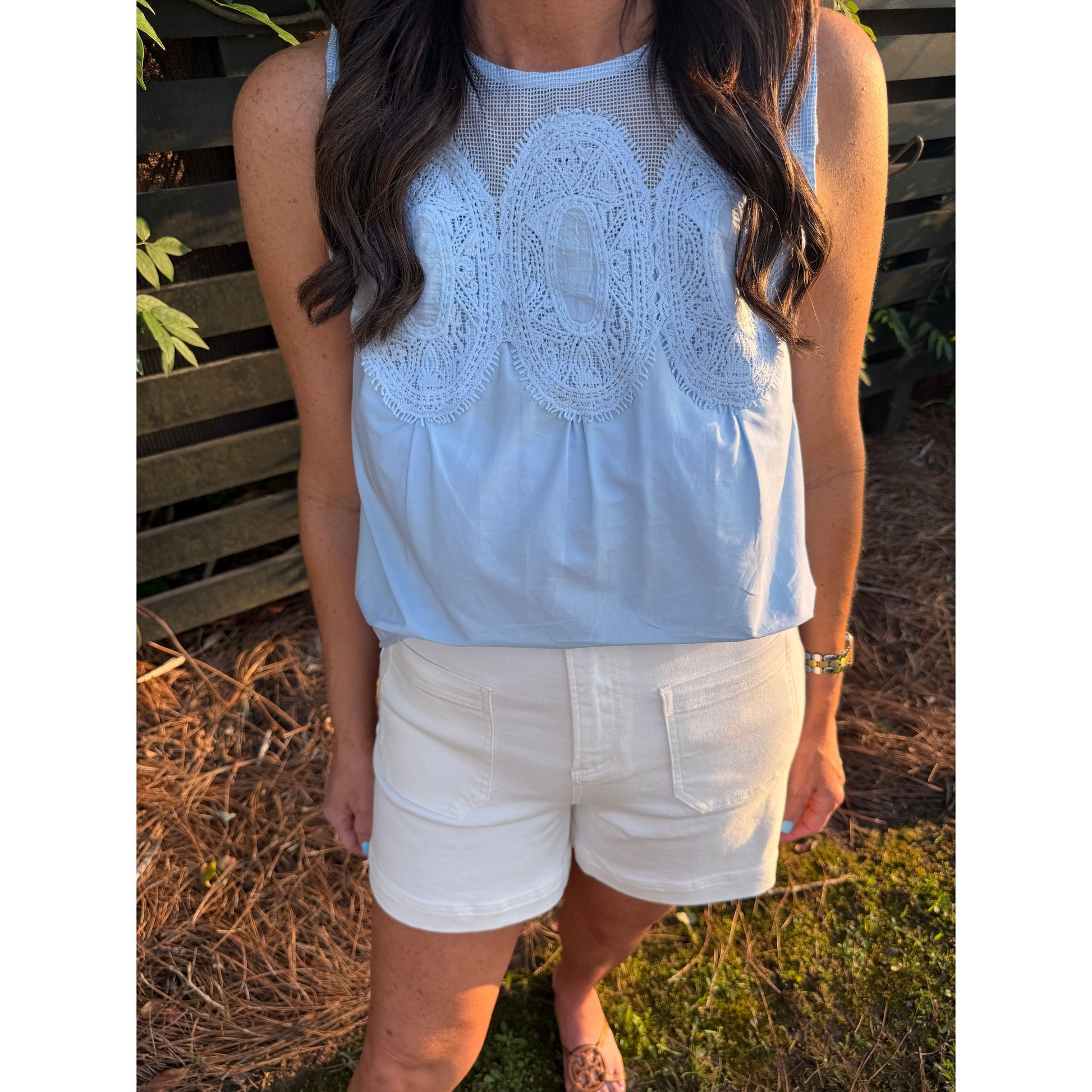 Person wearing a white sleeveless top with lace details and white pants outdoors.