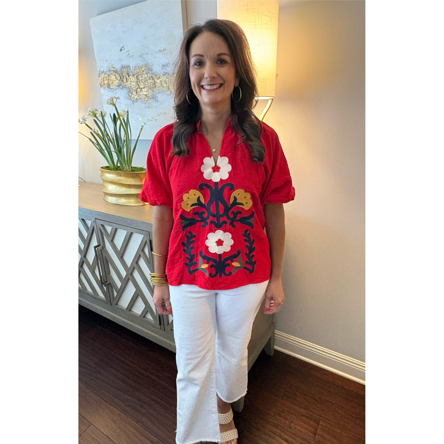 Woman wearing a red embroidered blouse with floral patterns in a room.