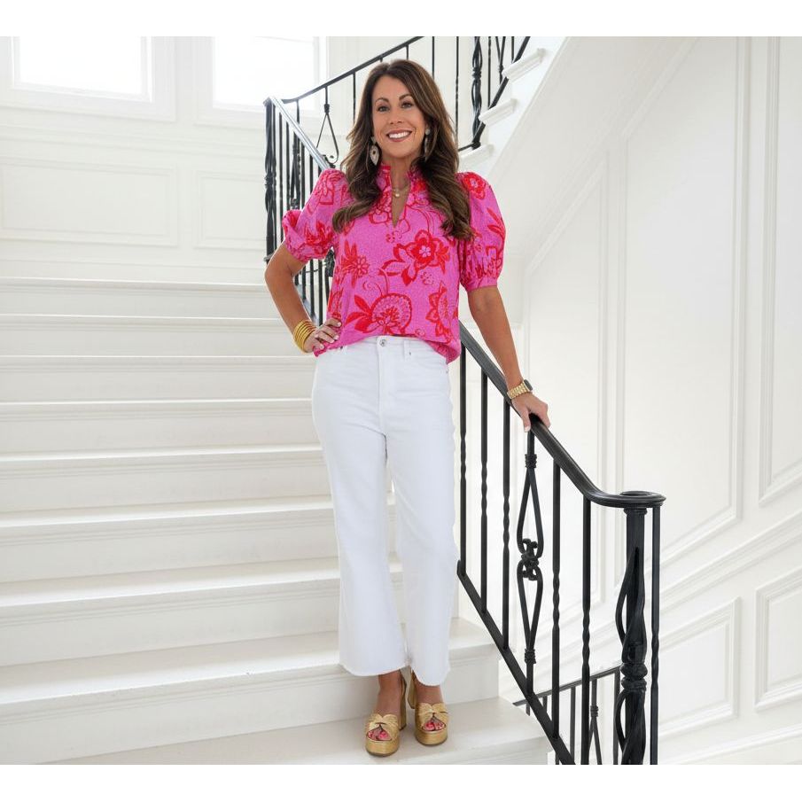 Woman in a pink floral blouse and white pants standing on a white staircase. 