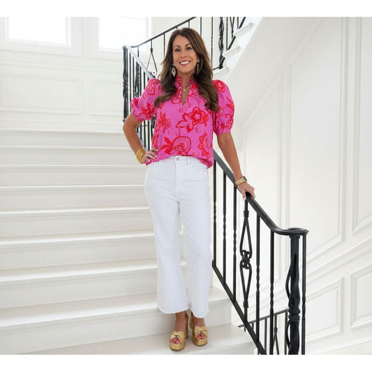 Woman in a pink floral blouse and white pants standing on a white staircase. 