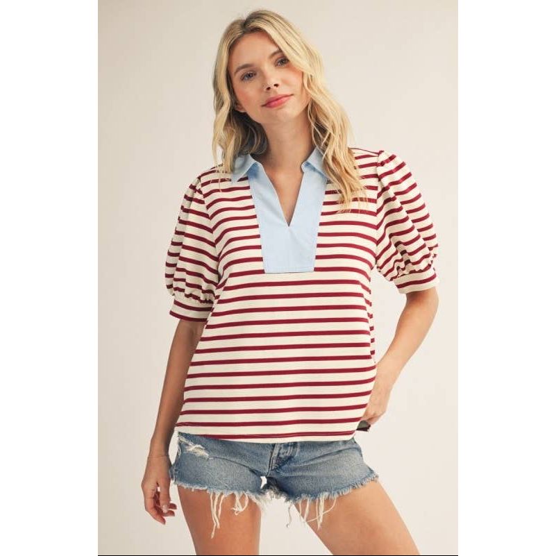 Woman wearing a red and white striped shirt with a light blue collar and denim shorts on a plain background