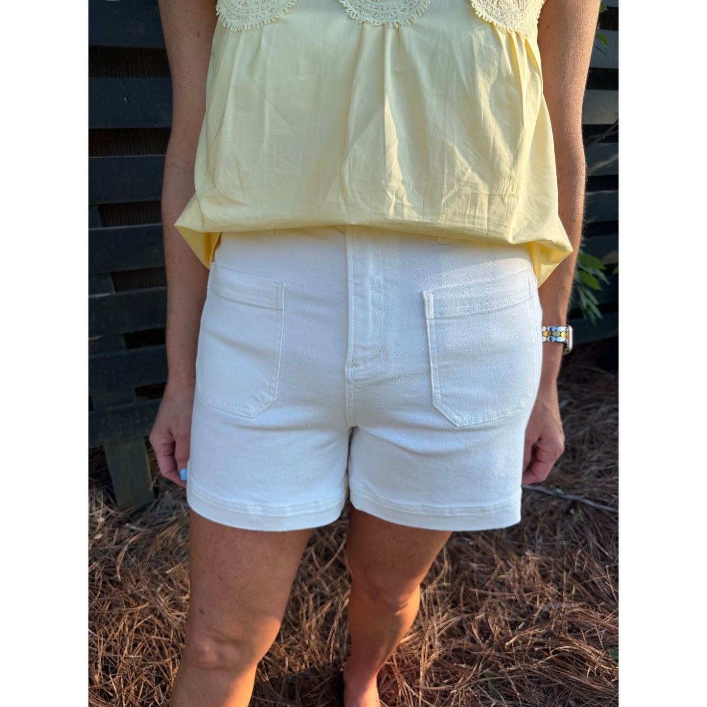 Person wearing a yellow top and white shorts standing outdoors.