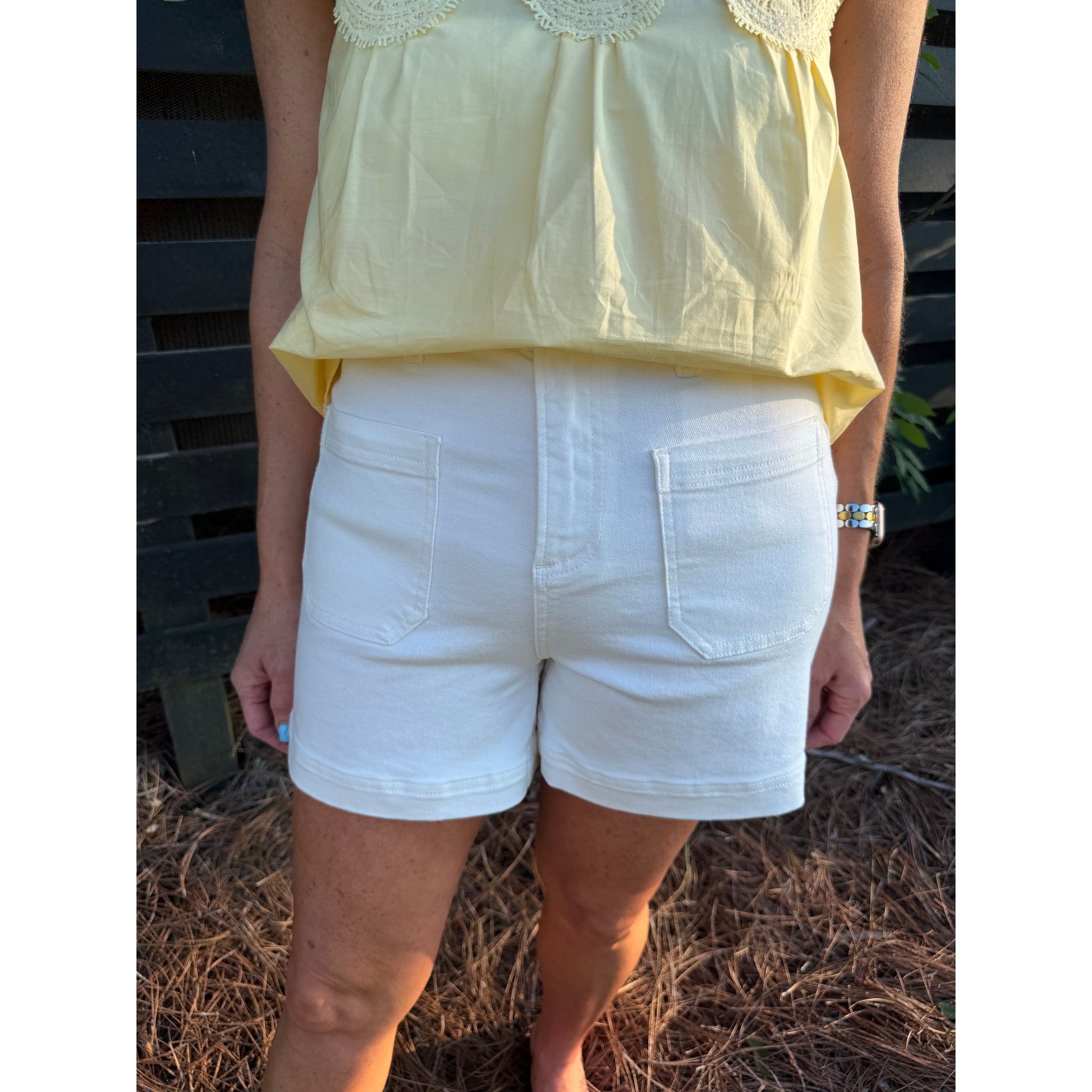 Person wearing a yellow top and white shorts standing outdoors.