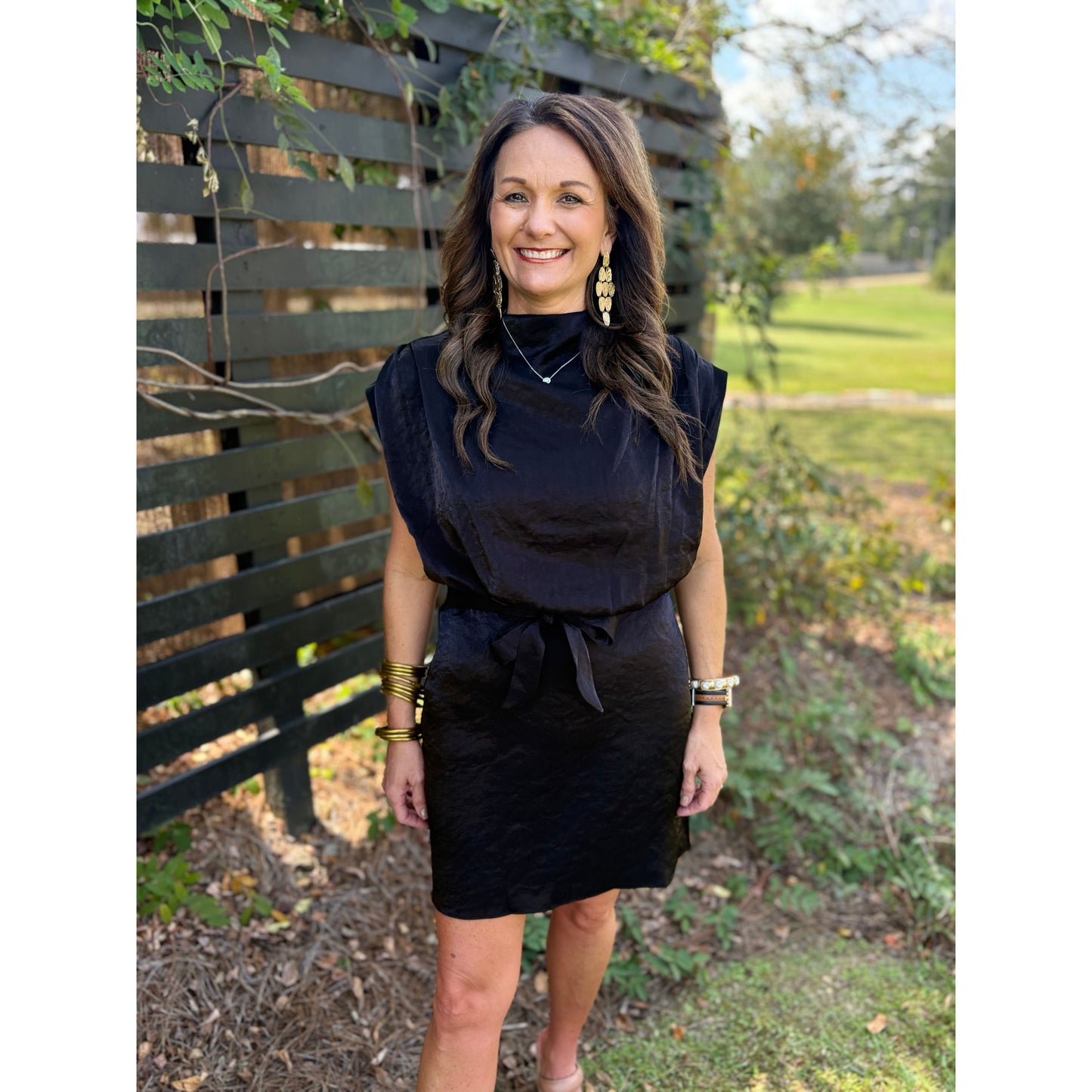 Woman wearing a black dress standing outdoors with greenery in the background