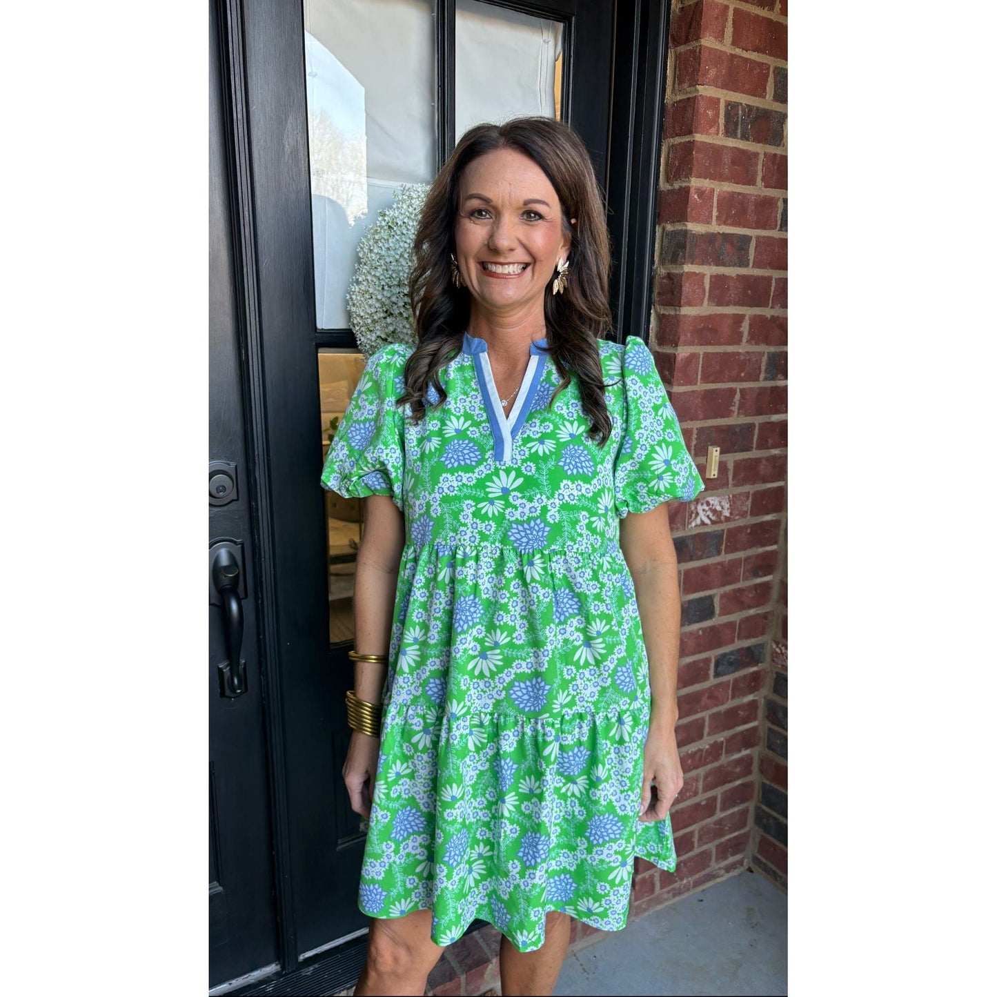 Woman in a green floral dress standing outside a house.
