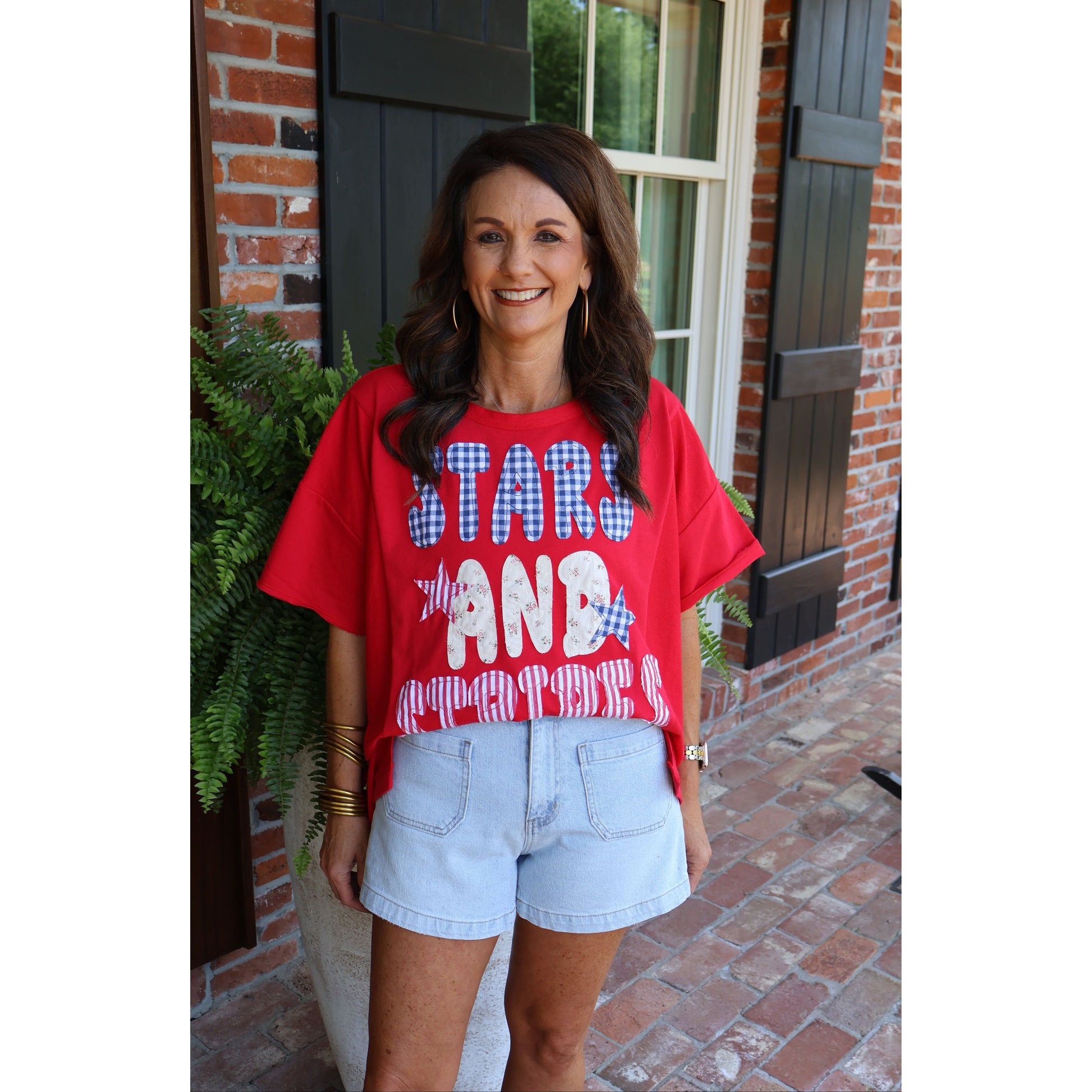 Woman wearing a red t-shirt with 'Stars and Stripes' design in front of a brick building.