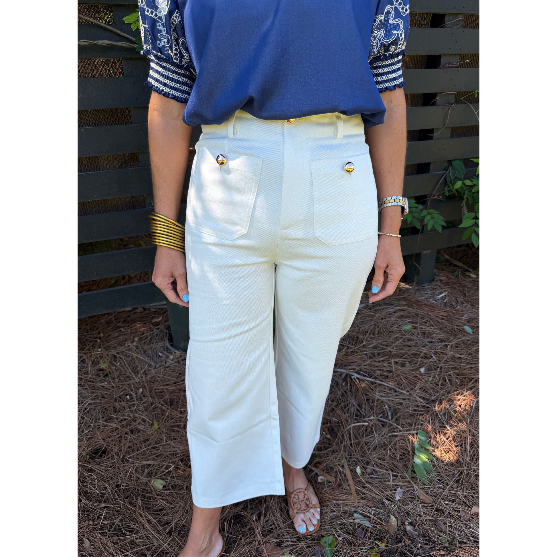 Person wearing white pants with gold buttons sitting on a bench outdoors.