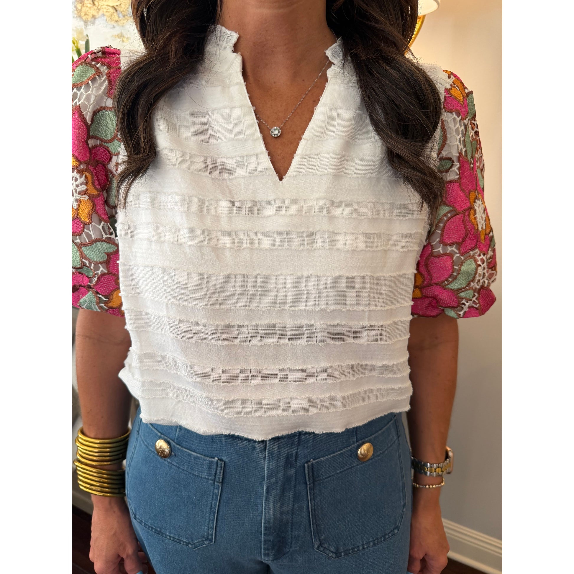Person wearing a white shirt and blue shorts with floral top and yellow bracelet.