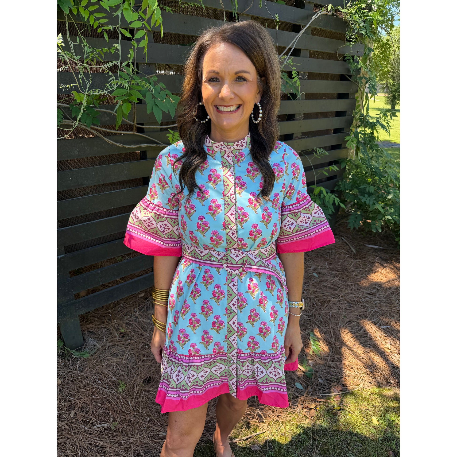 Woman wearing a colorful dress standing outdoors with greenery in the background