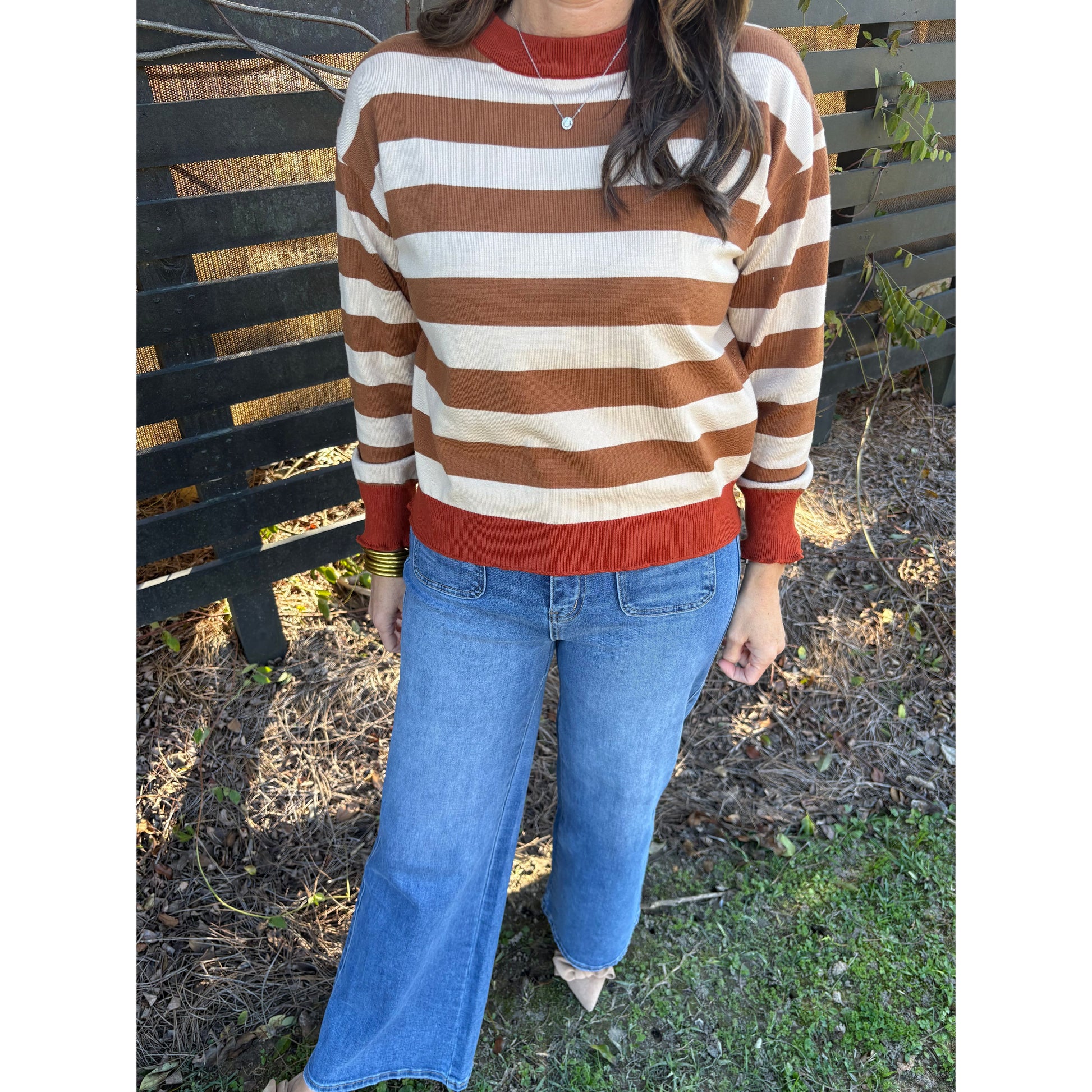 Person wearing a striped sweater and blue jeans sitting on a bench outdoors.