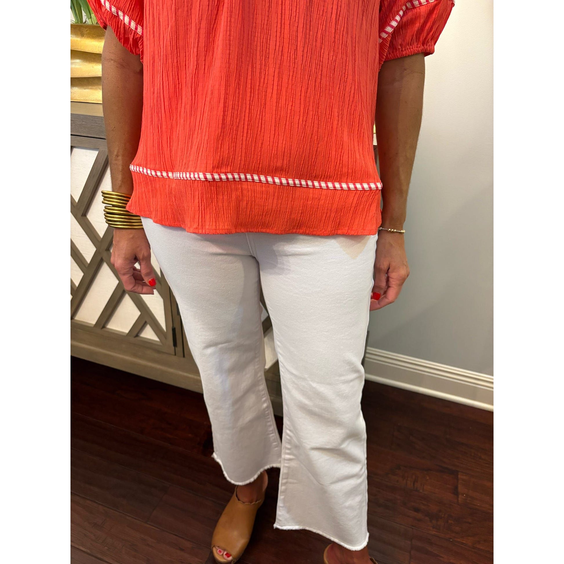 Person wearing a red blouse with white trim and white pants indoors.