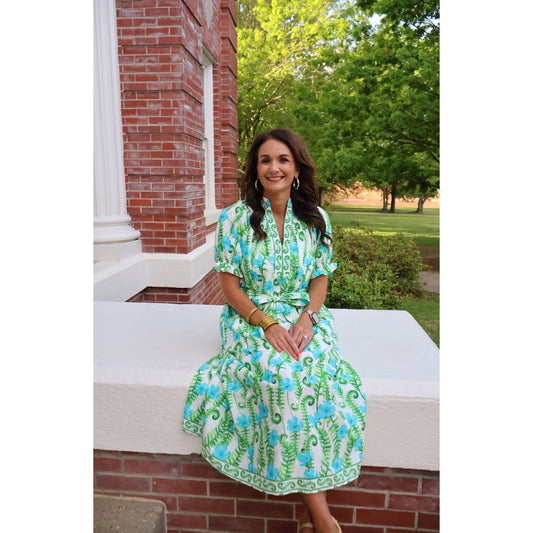 Woman in a green floral dress sitting on a bench outdoors.