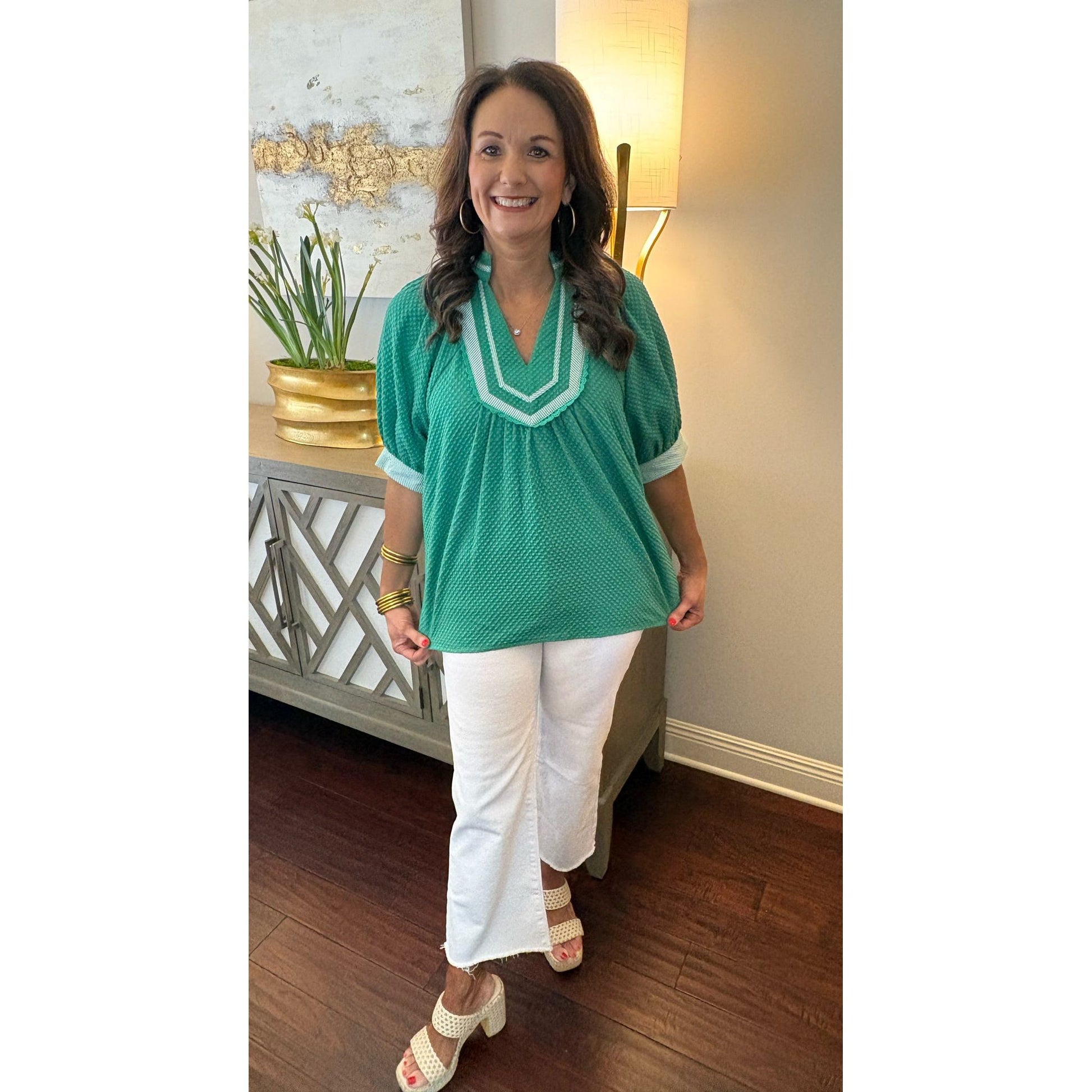 Woman wearing a green top and white pants in an indoor setting
