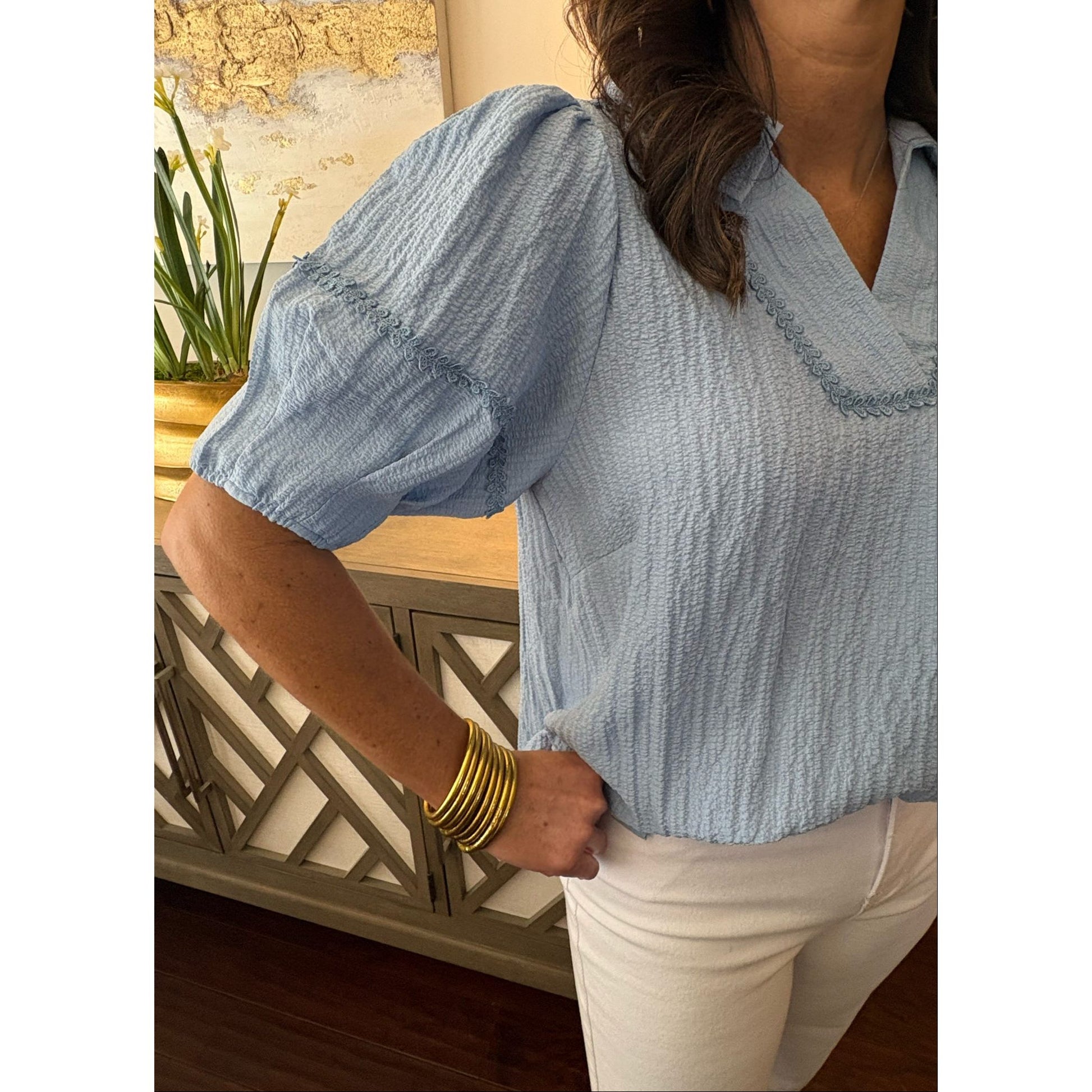 Person wearing a light blue textured blouse with a neutral background