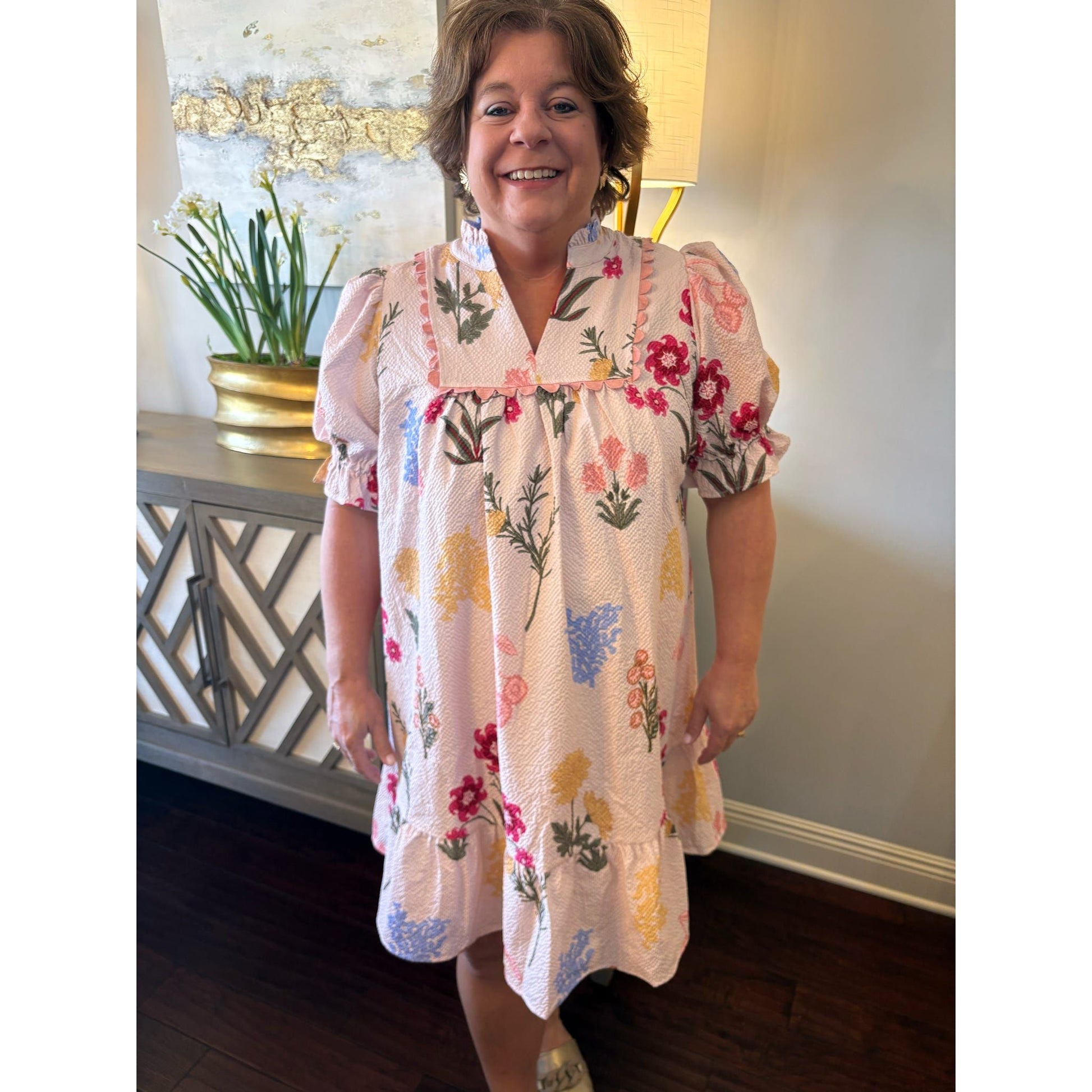 Woman wearing a floral dress standing indoors with decorative elements in the background