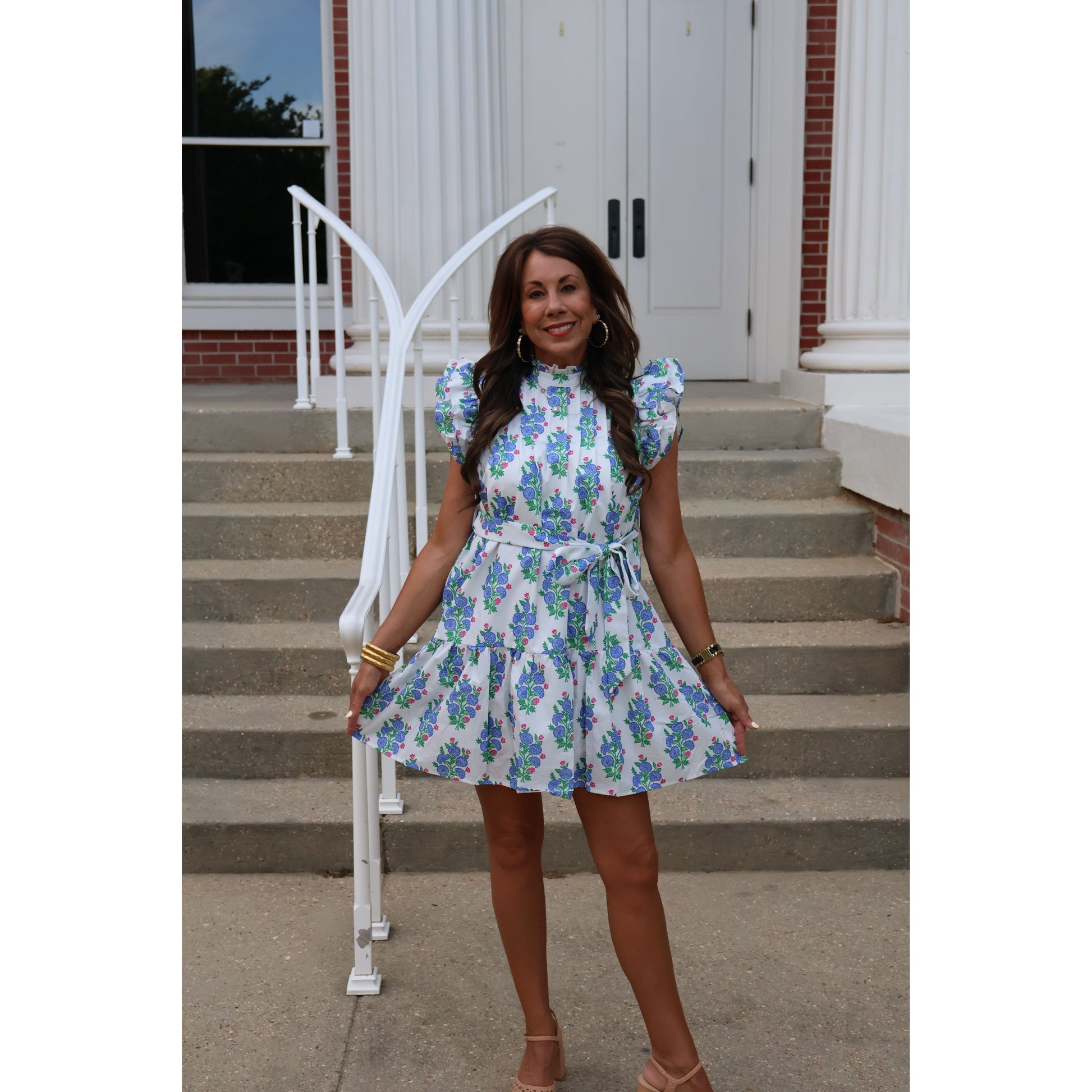 Woman in a floral dress standing on steps with a white chair and door in the background